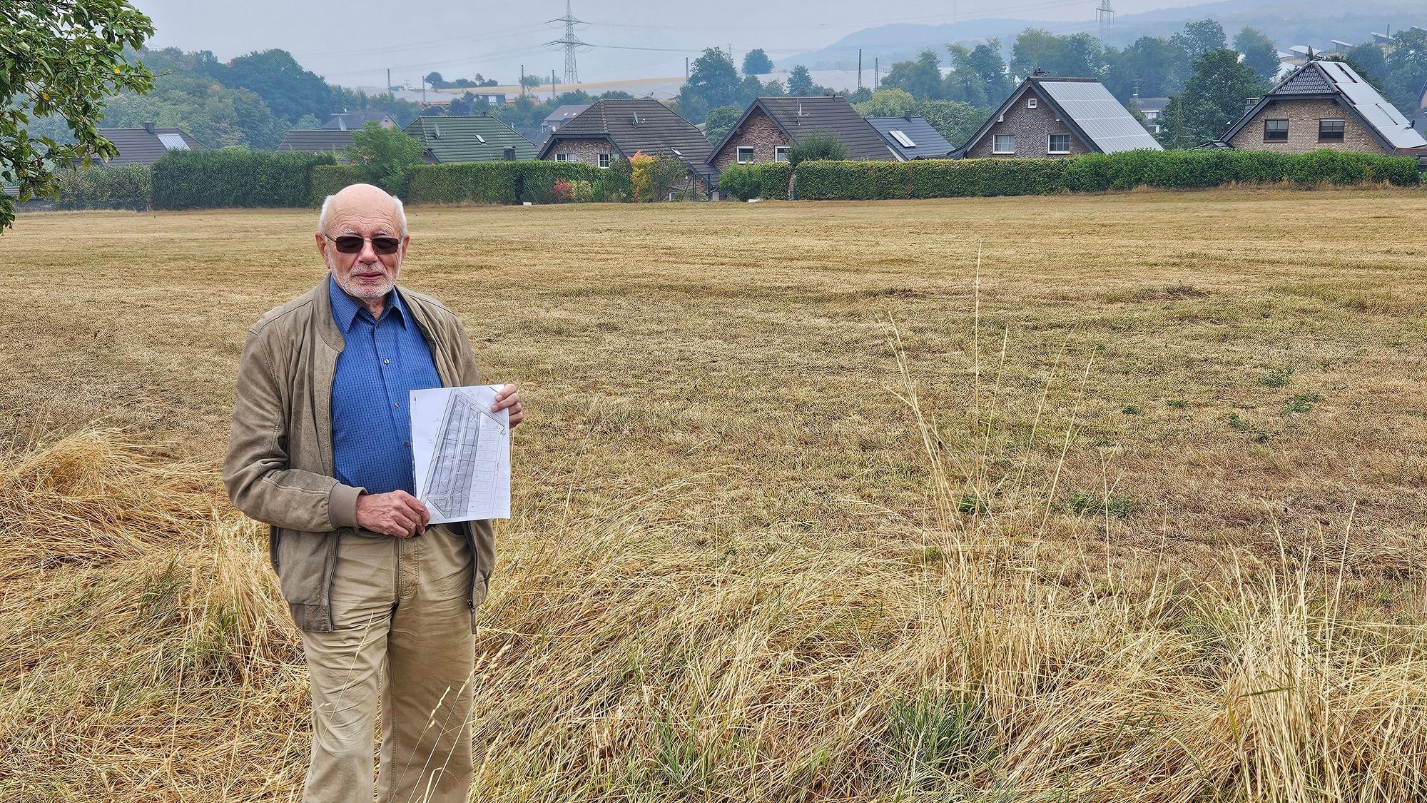 Hans Reiff steht mit einem Plan vor einer Wiese. Im Hintergrund sind Häuser zu sehen.