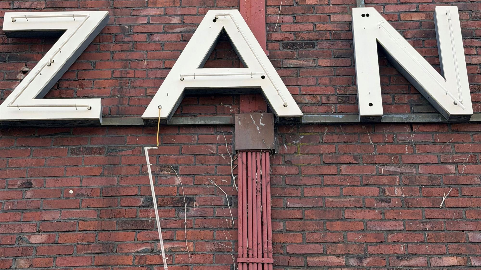 Leuchtstoffröhren hängen zerstört vom Schriftzug „Gohrsmühle Zanders“ herunter.