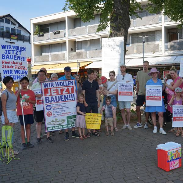 Menschen im Halbrund mit Protestplakaten, Aufschrift "Wir wollen jetzt bauen"