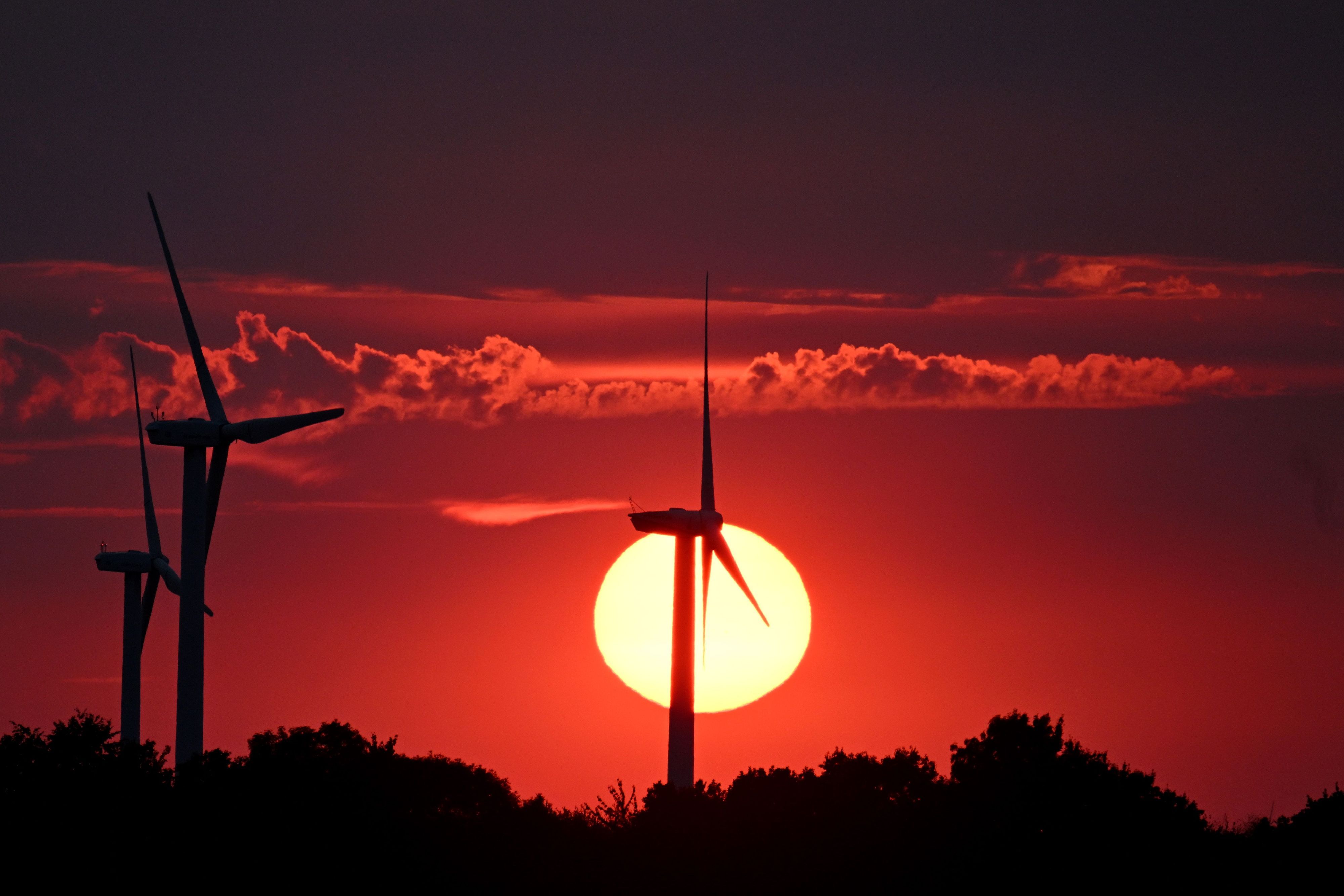 Hinter Windrädern färbt die sinkende Sonne den Himmel rot.