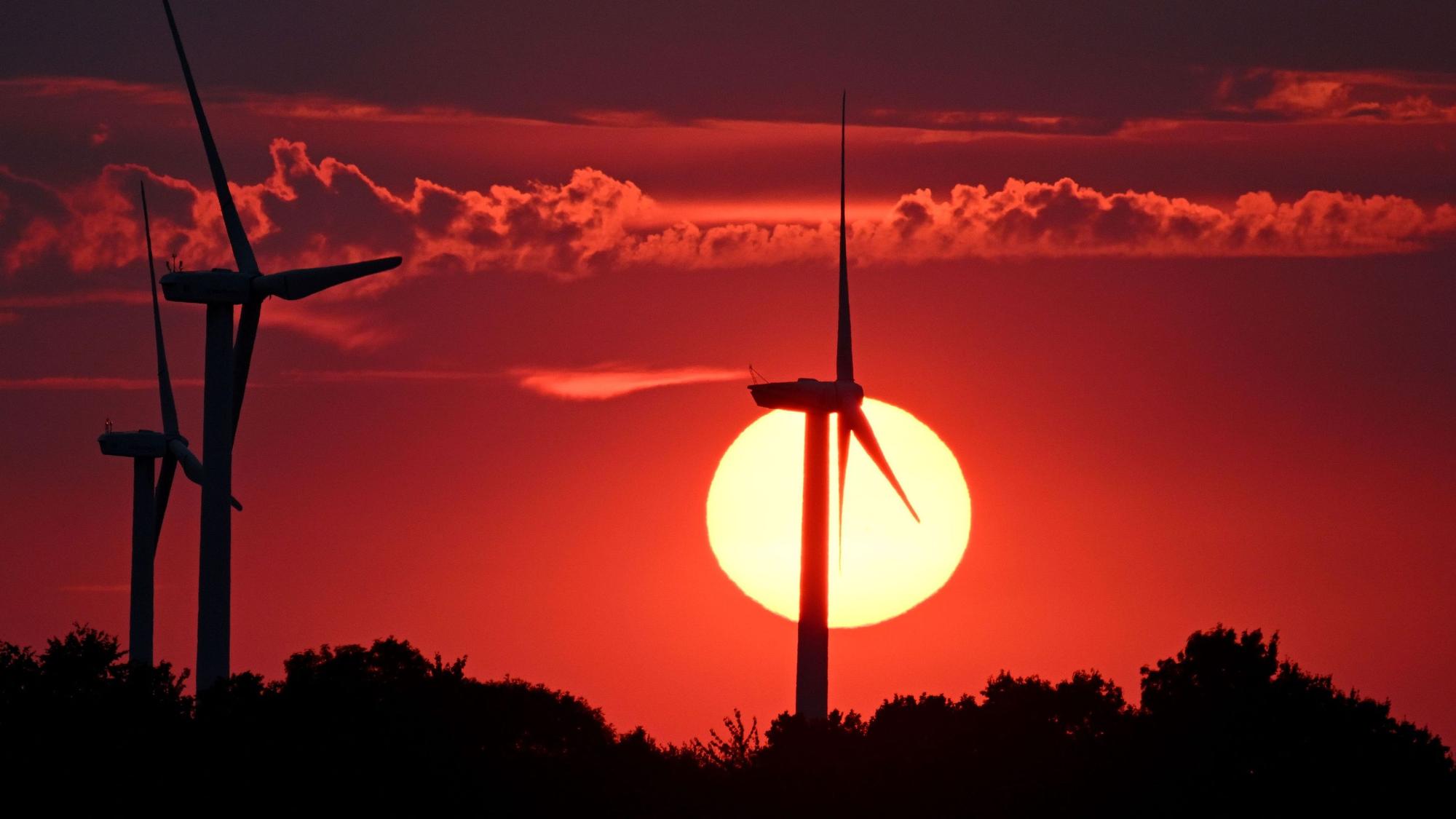 Hinter Windrädern färbt die sinkende Sonne den Himmel rot.