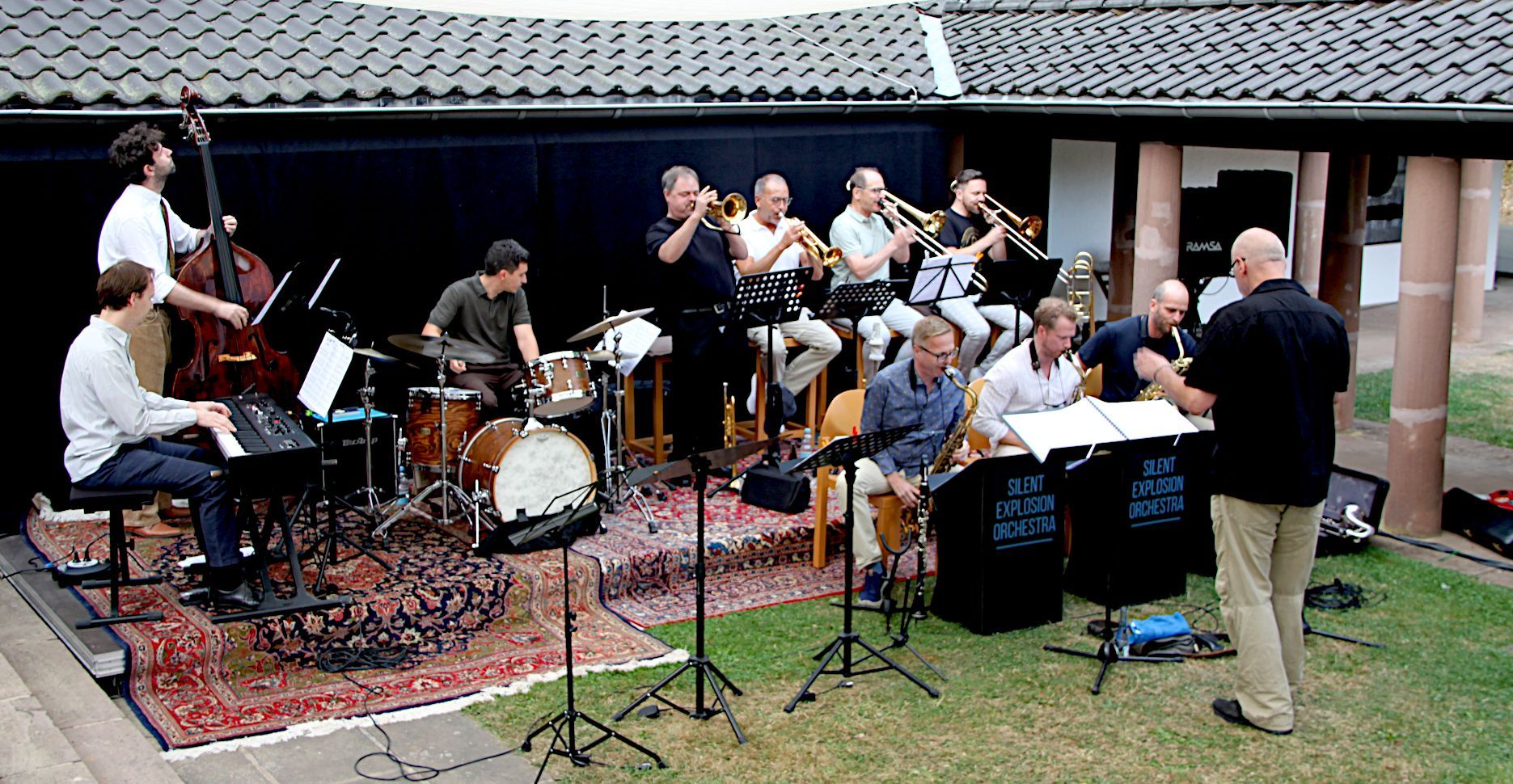 Eine Band mit zehn Musikern spielt auf einer improvisierten Bühne.
