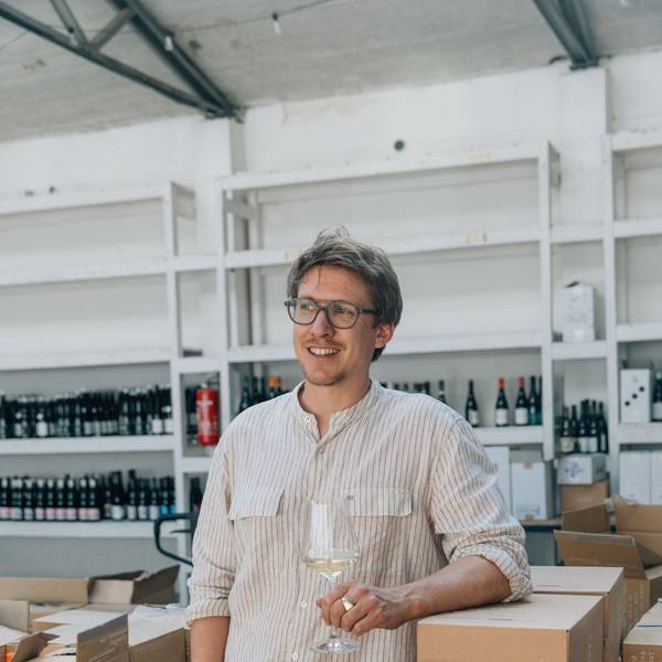 Fabian Lay steht mit einem Weinglas in der Hand vor einem Weinregal.