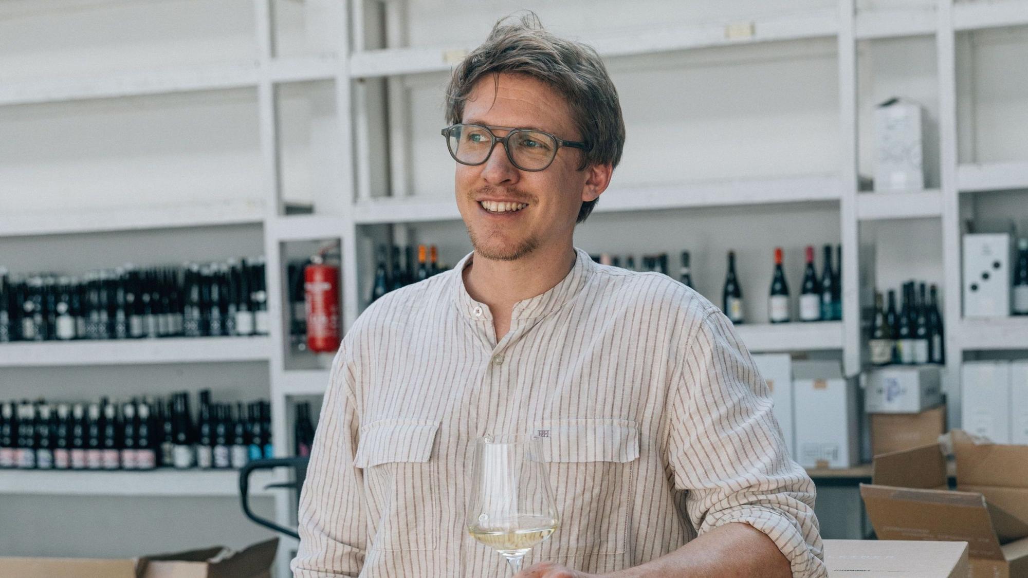 Fabian Lay steht mit einem Weinglas in der Hand vor einem Weinregal.
