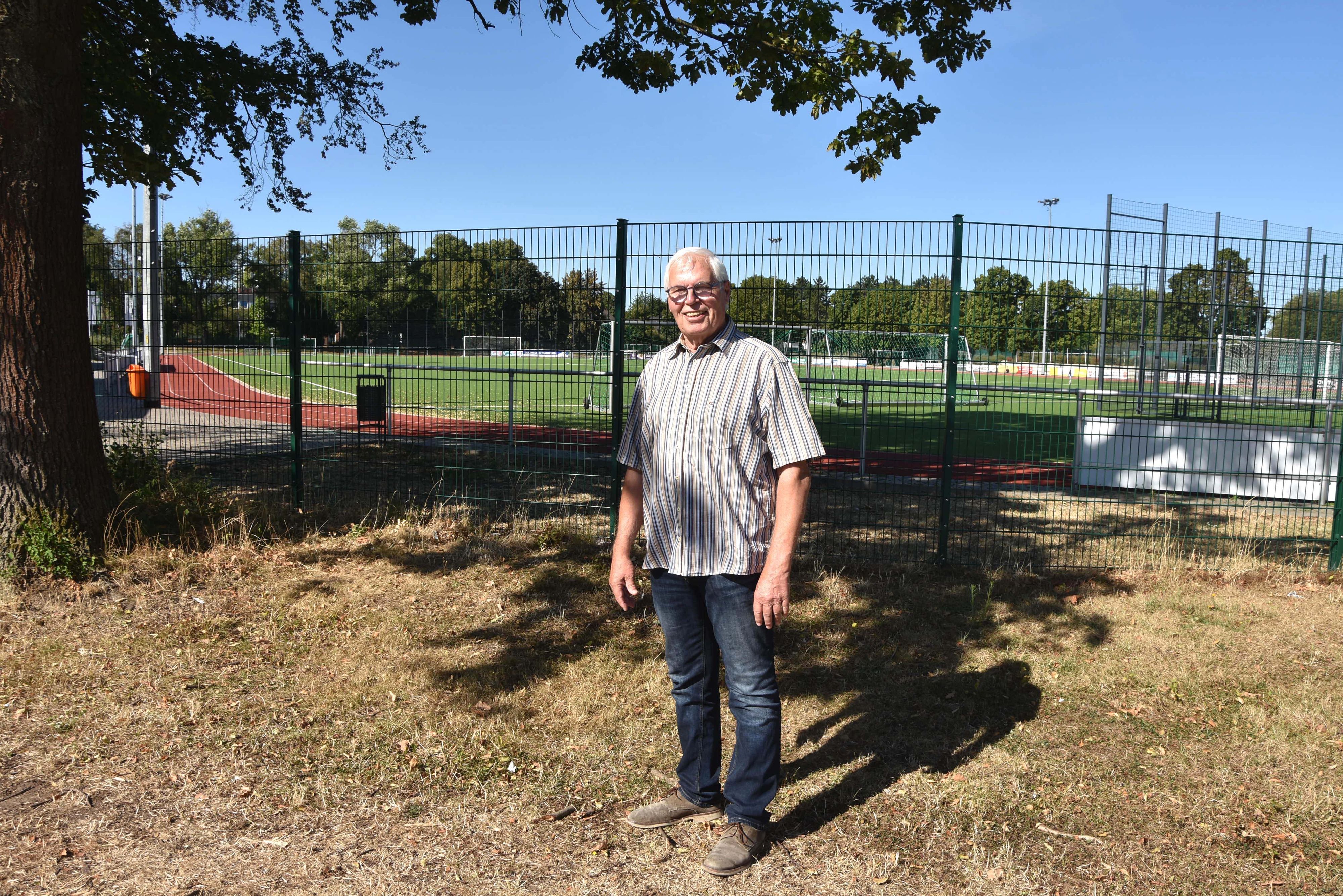 Das Foto zeigt einen Mann vor einem Sportplatz.
