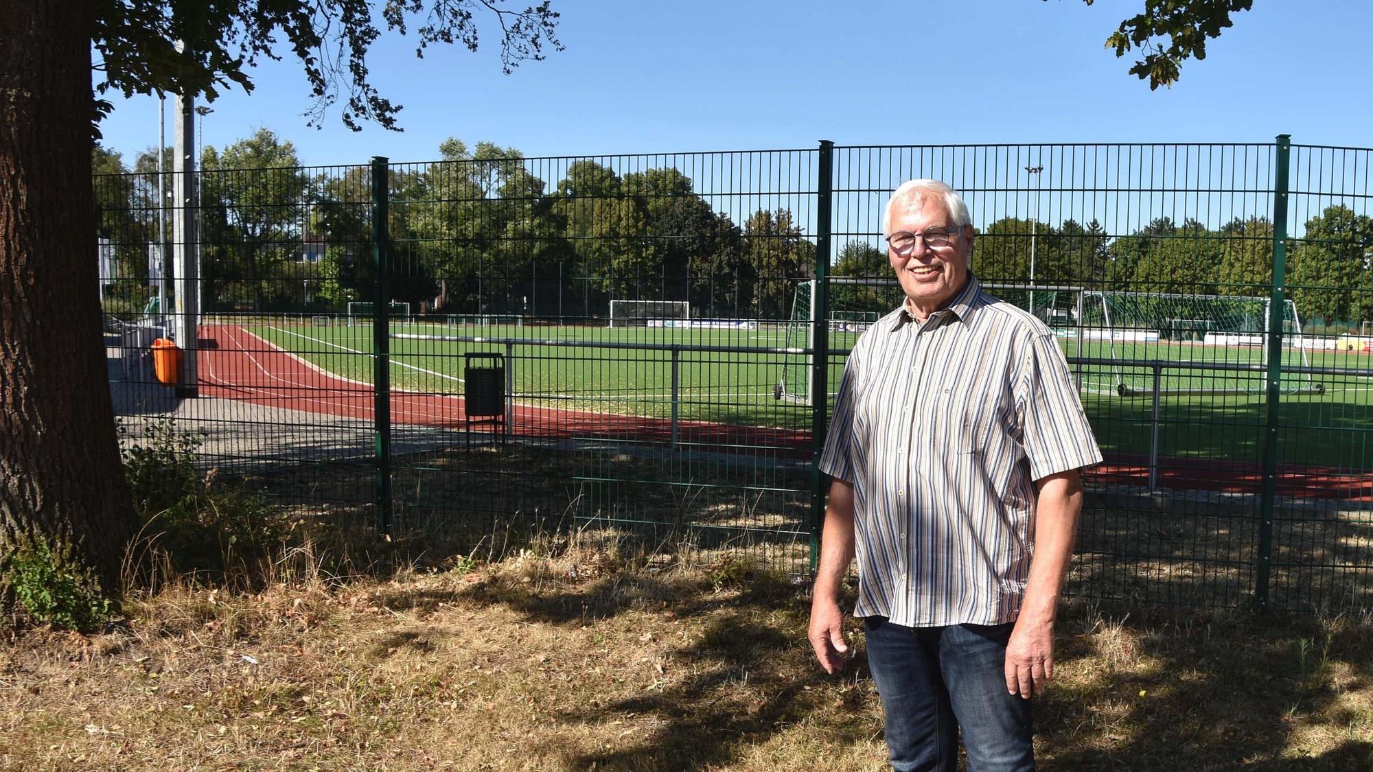 Das Foto zeigt einen Mann vor einem Sportplatz.