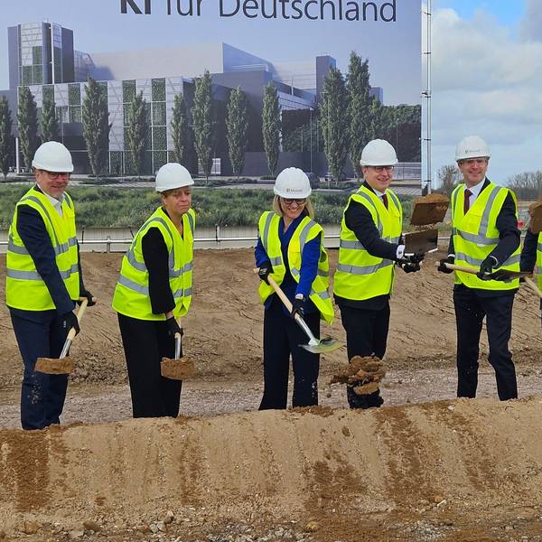 Zu sehen sind Menschen in Schutzwesten und mit Helmen bei einem Spatenstich.