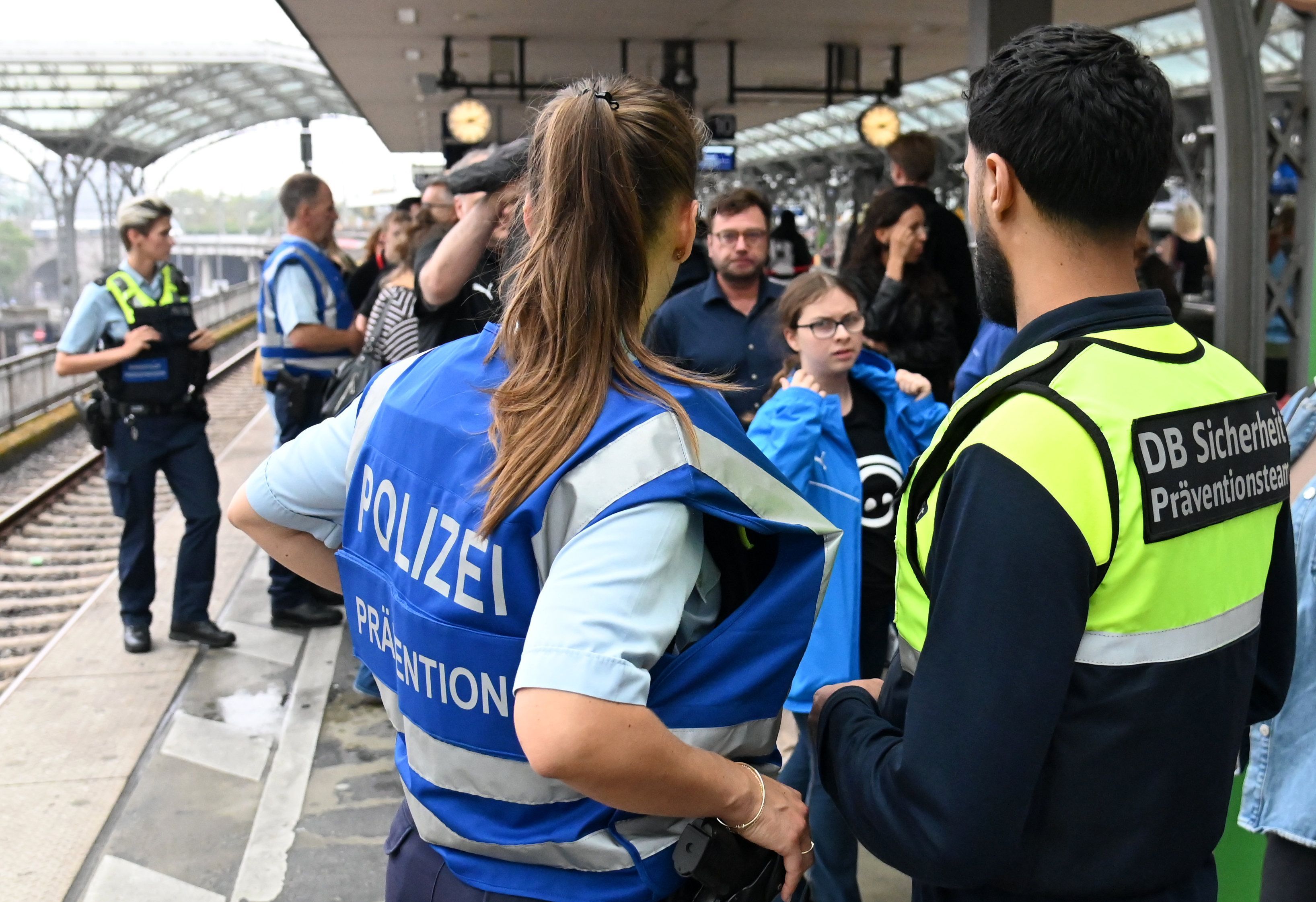 Zwei Sicherheitsbeamte der Deutschen Bahn und der Polizei stehen an einem vollen Bahngleis mit dem Rücken zur Kamera.