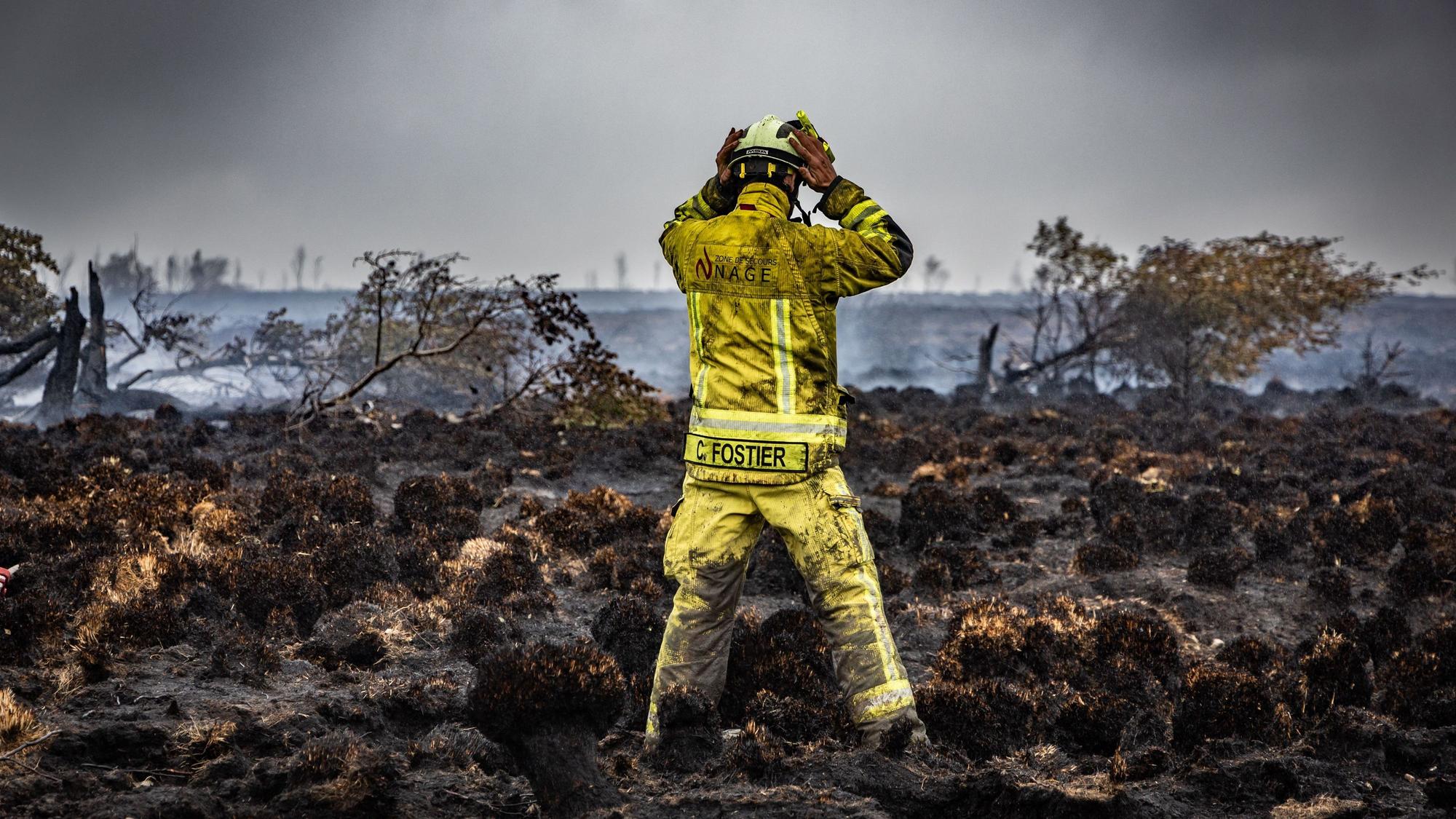 Ein Feuerwehrmann steht auf der verkohlten Erde eines Waldbrandes.
