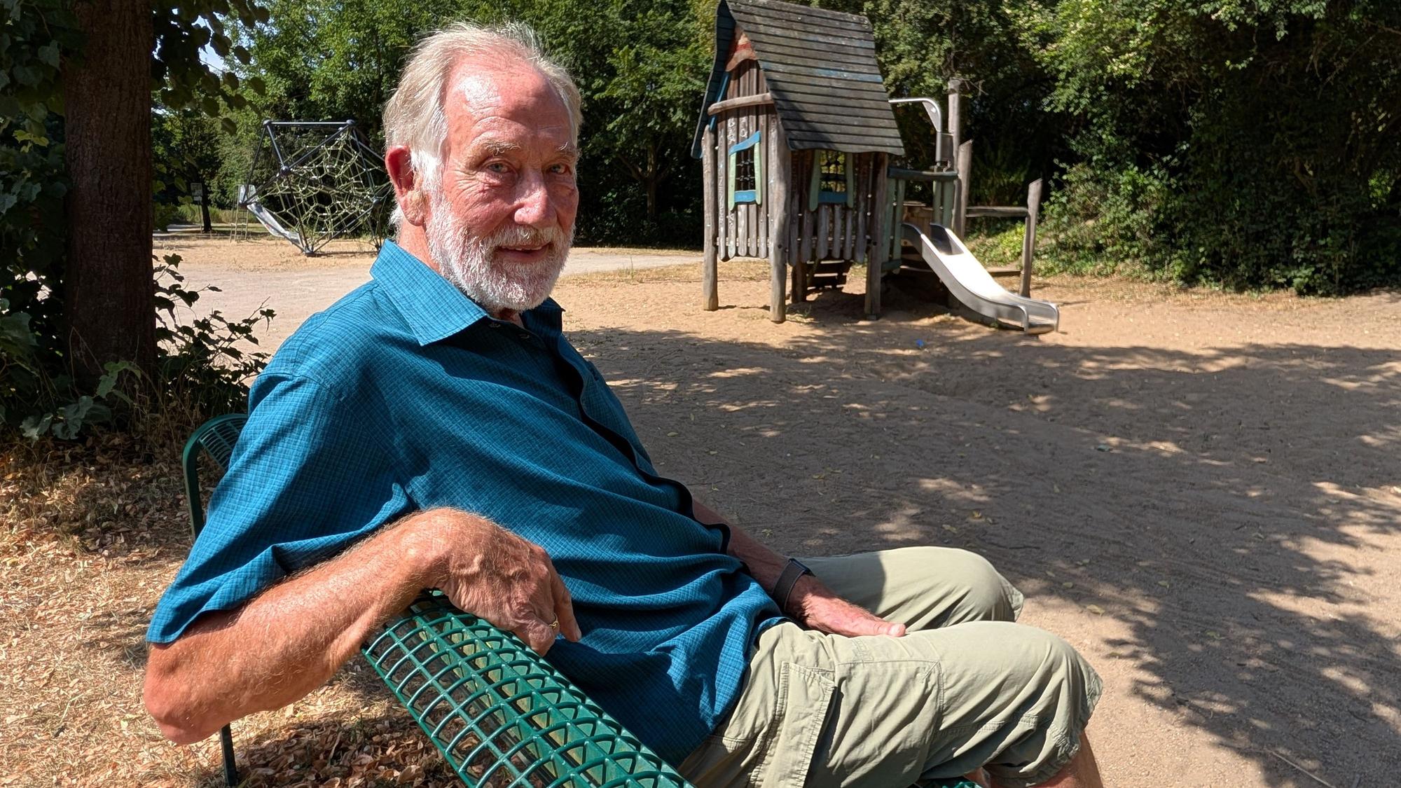 Das Foto zeigt einen Mann, der auf einer Bank sitzt.