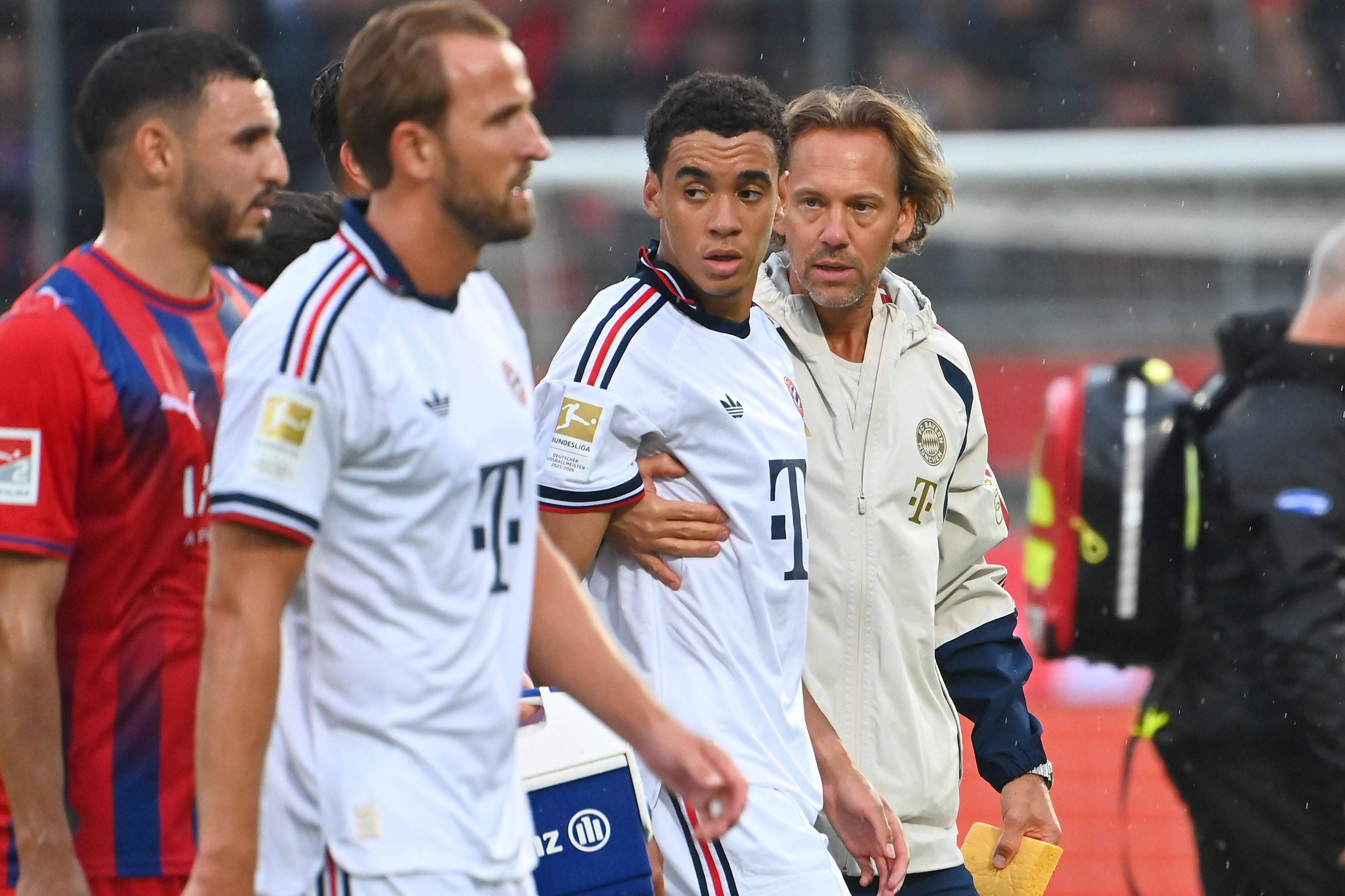 Jamal MUSIALA Bayern Muenchen bricht erneut zusammen,Ohnmacht, wird von Dr.Peter UEBLACKER Mannschaftsarzt FCB vom Platz gefuehrt, li:Harry KANE Bayern Muenchen. Fussball Testpiel / 1.FC Heidenheim - FC Bayern Muenchen 2-5 am 18.08.2025 , VOITH ARENA. *** Jamal MUSIALA of Bayern Munich collapses again,faints, is led off the field by Dr. Peter UEBLACKER, FCB team doctor featuring Harry KANE, Bayern Munich soccer friendly match: FC Heidenheim 1, FC Bayern Munich 2-5 on August 18, 2025, at VOITH ARENA