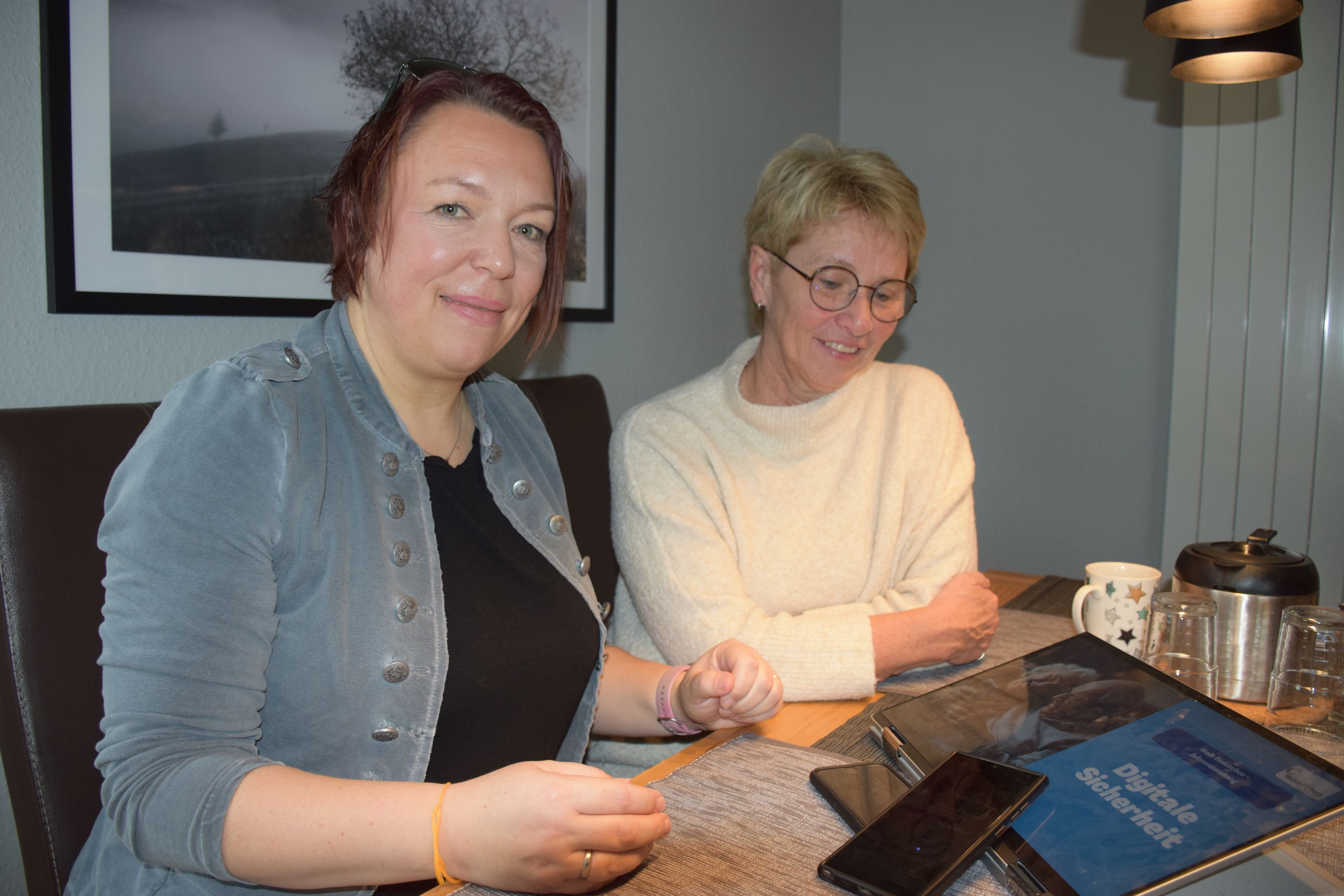 Zwei Frauen sitzen an einem Tisch, vor ihnen liegen ein Tablet und ein Smartphone.