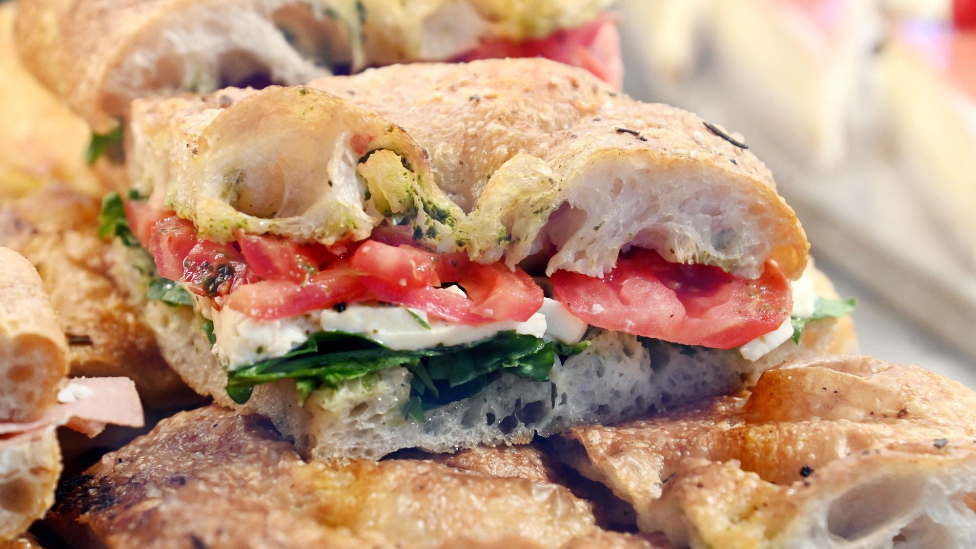 Ein Focaccia-Stück mit Tomaten, Mozzarella und Pesto liegt in der Auslage.