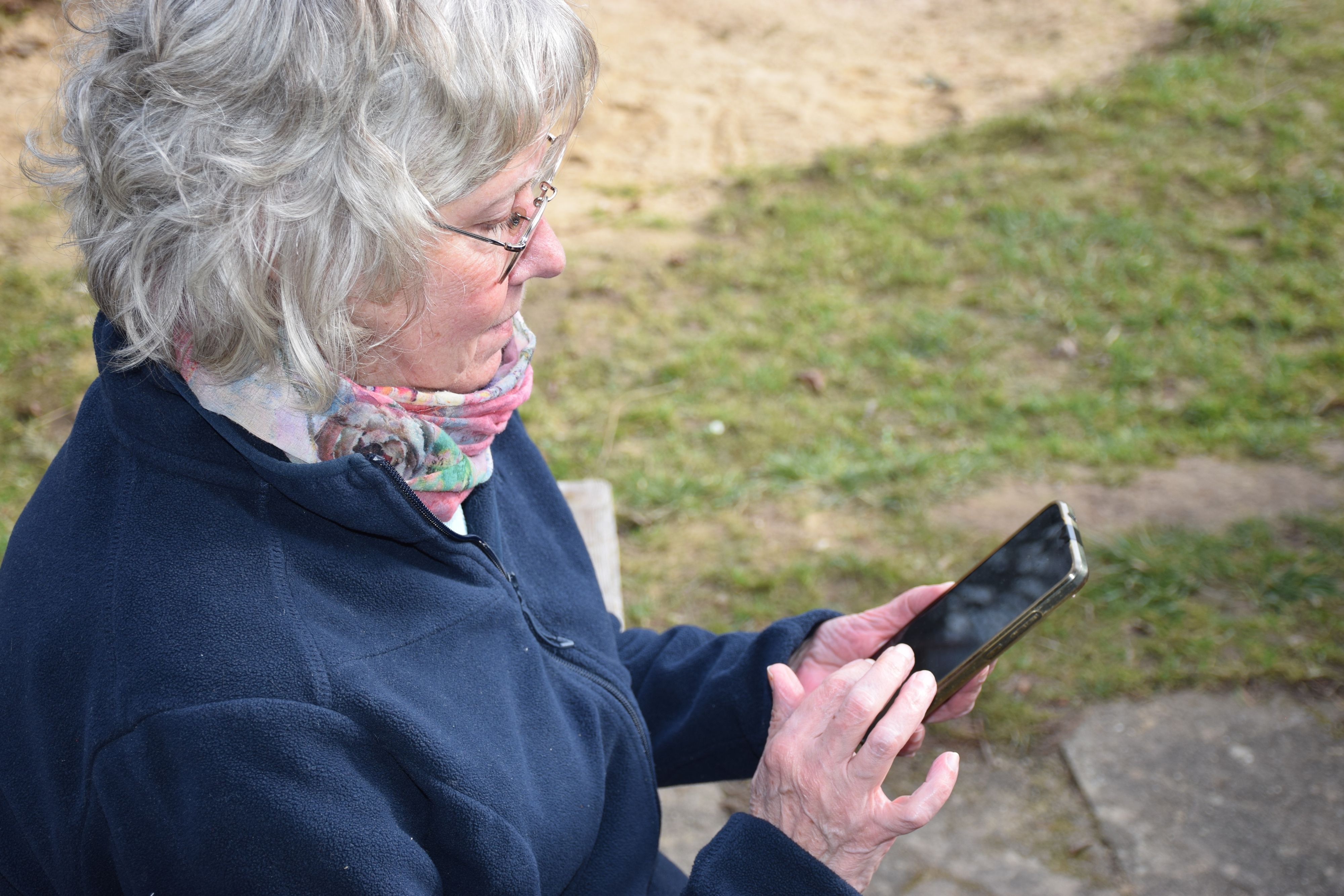 Eine Frau mit grauen Haaren hält ein Smartphone in der Hand und tippt auf dem Bildschirm.