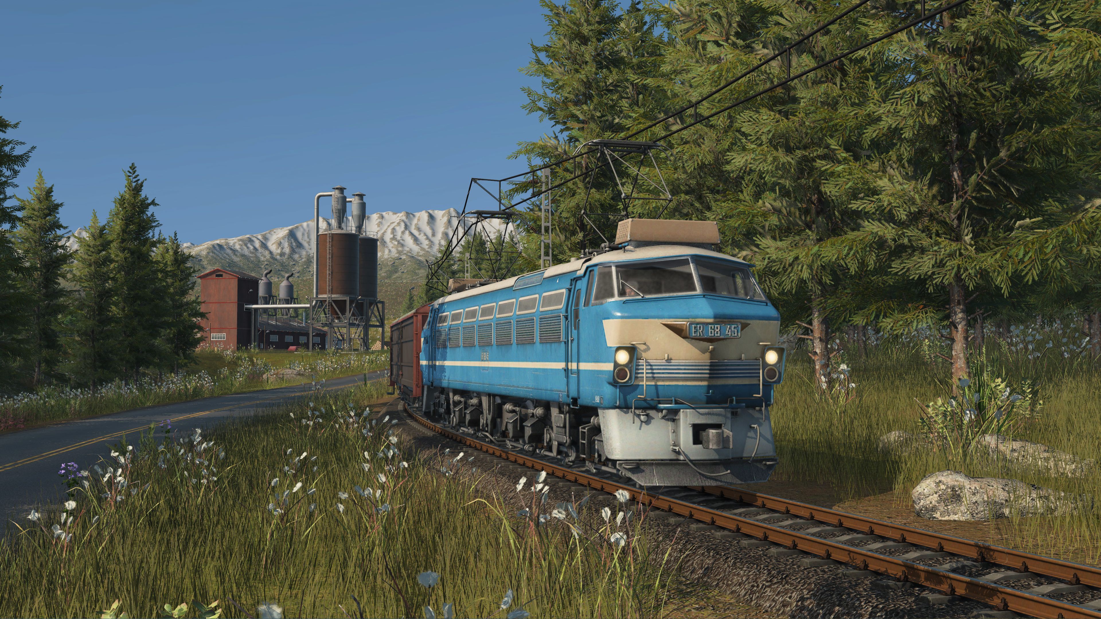 Szene aus „Transport Fever 3“: Eine blaue Eisenbahn in einer Waldlandschaft