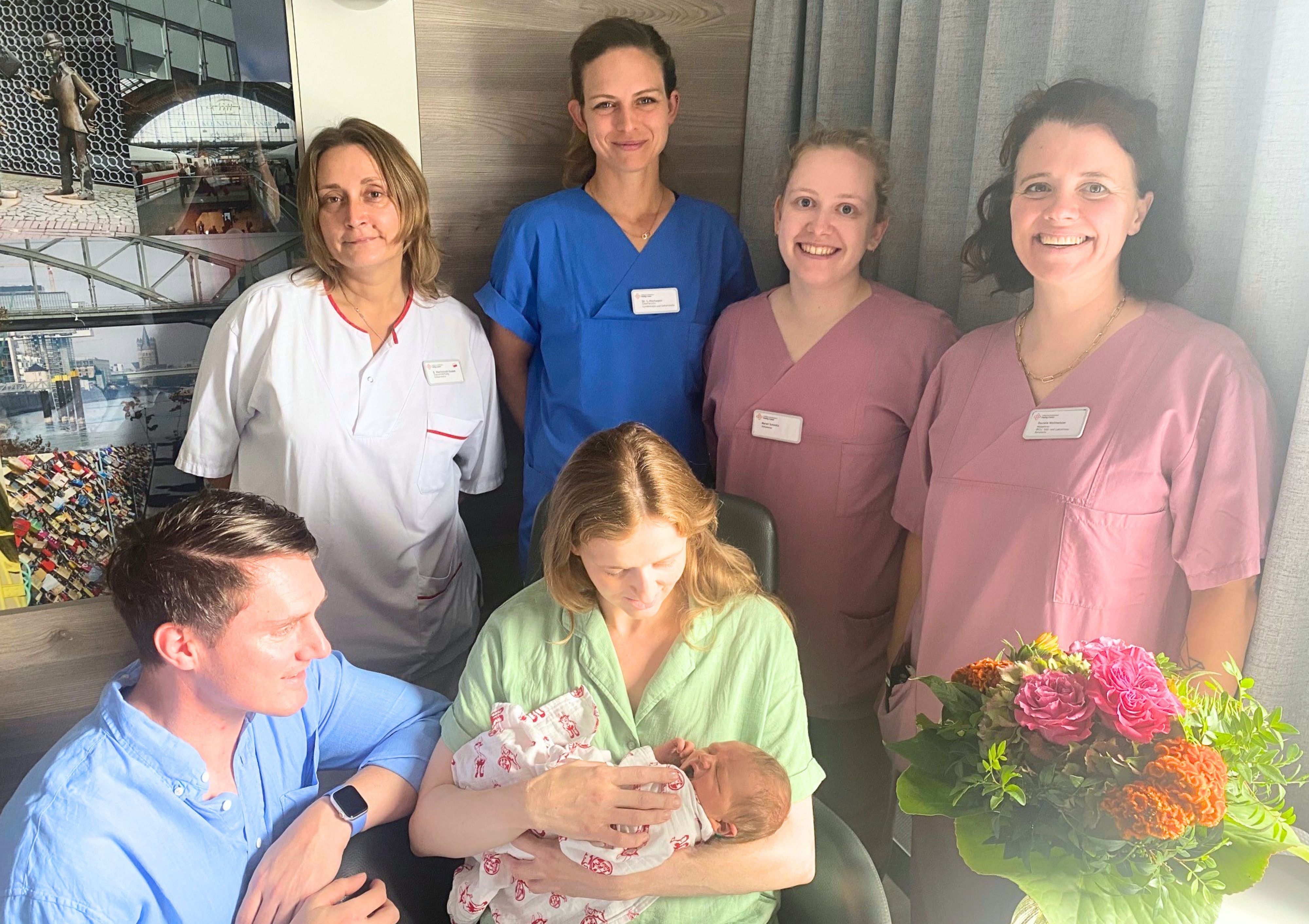 Baby Louis liegt in den Armen seiner Mutter. Daneben sind sein Vater sowie vier Mitarbeiter der Klinik zu sehen.