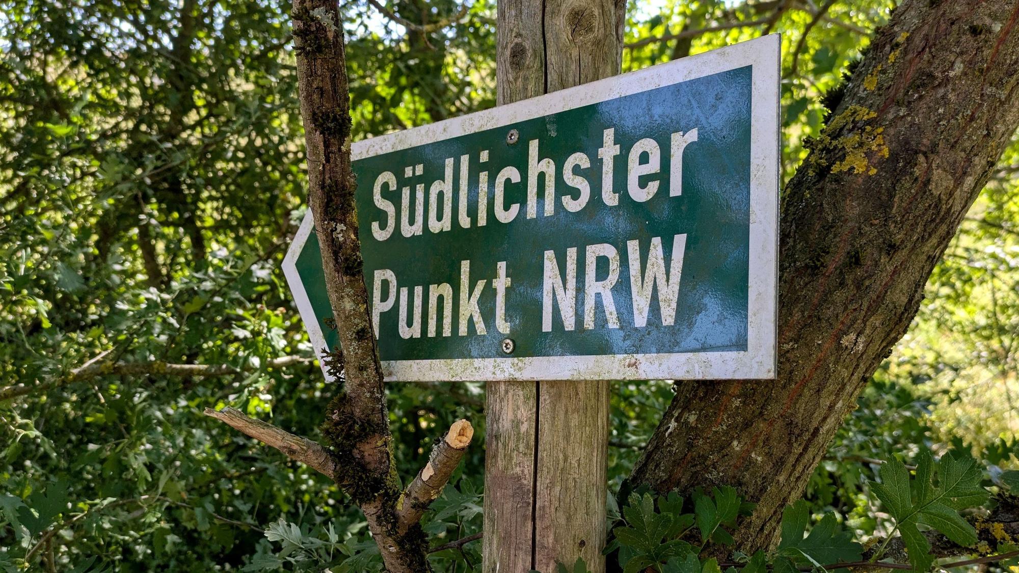 Ein grünes Hinweisschild mit weißer Schrift, das an einem Baum lehnt, weist den Weg zum südlichsten Punkt in NRW.