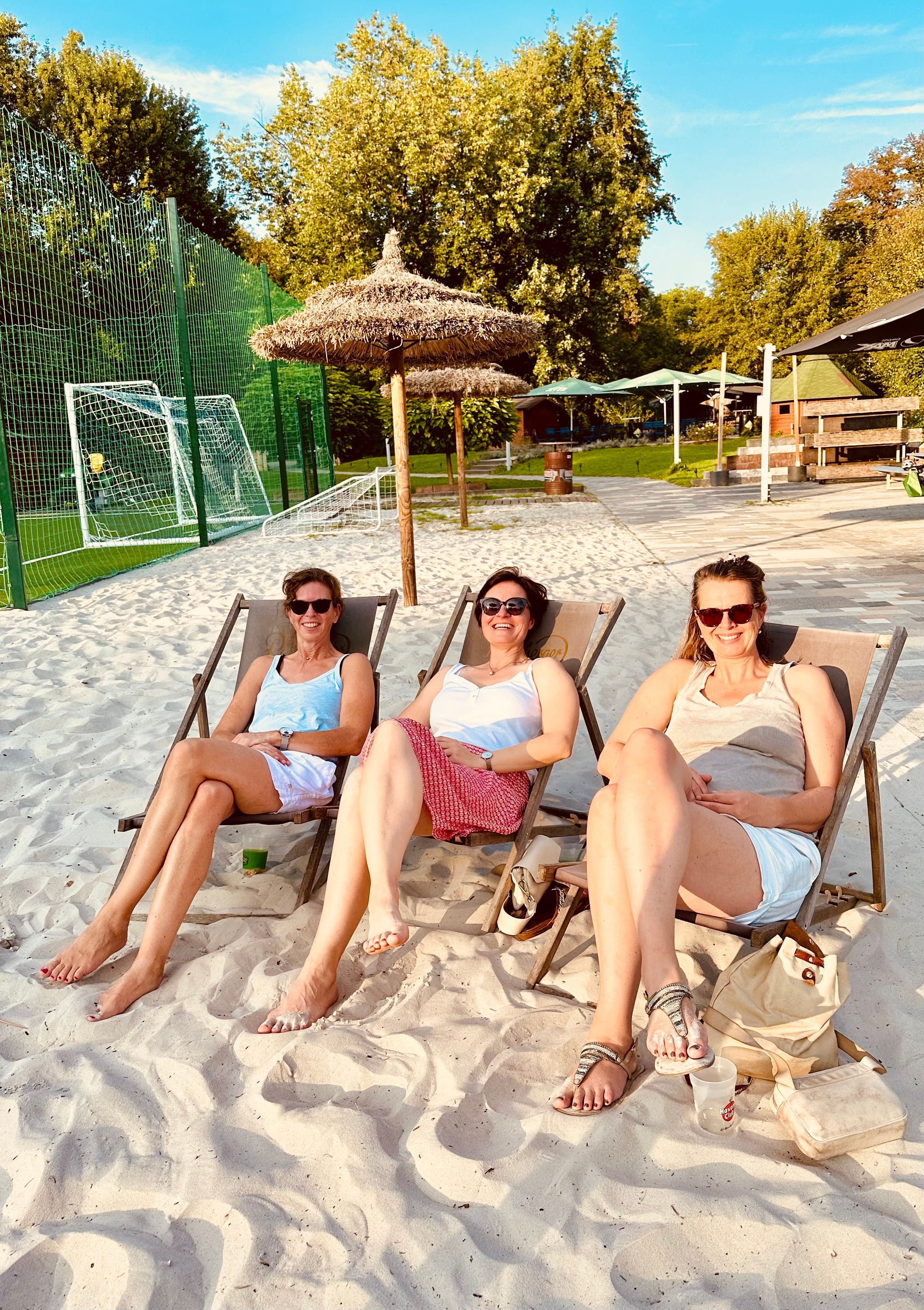 Zu sehen sind drei Frauen auf Strandstühlen auf einem Beachvolleyball-Feld.