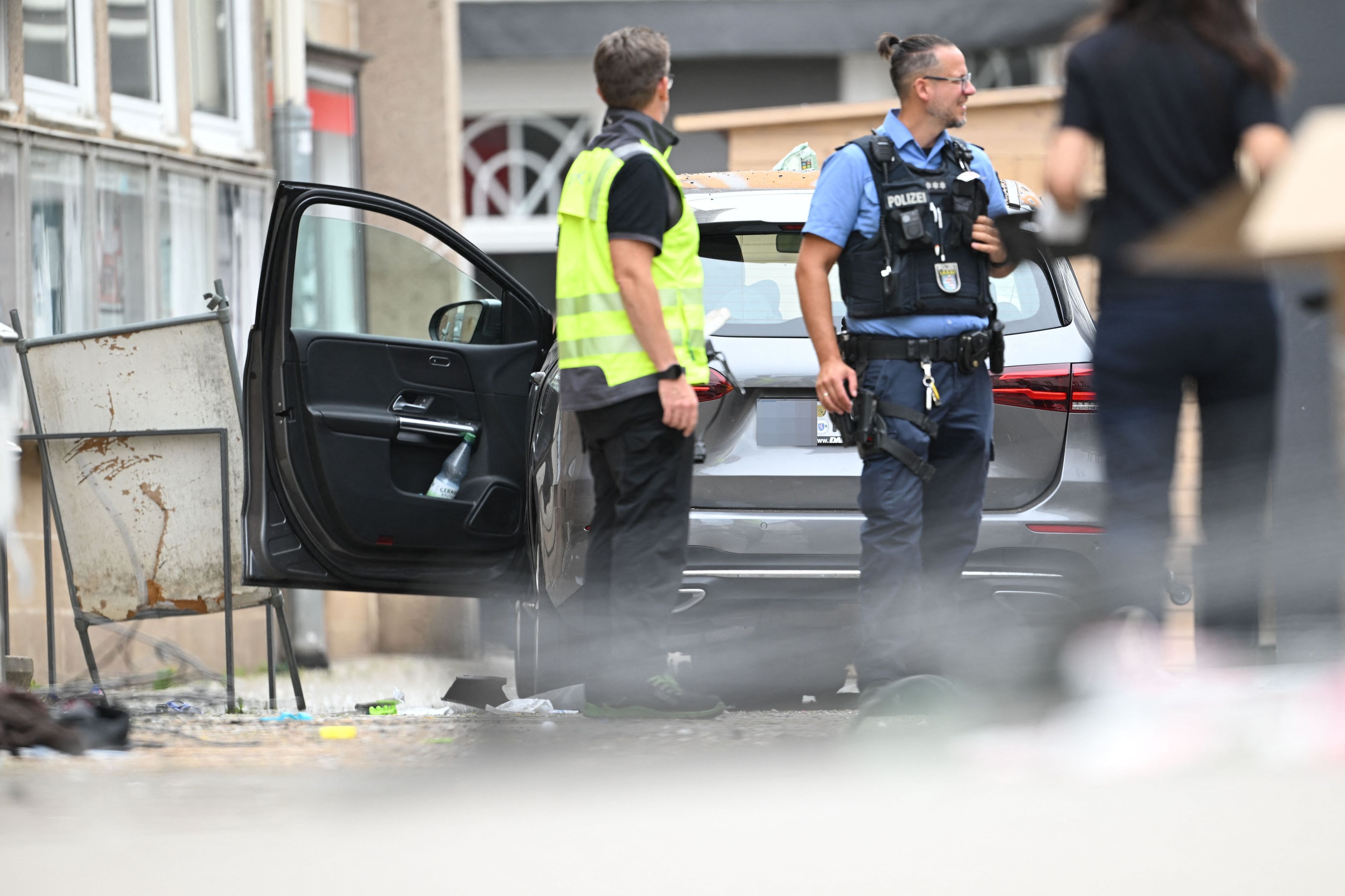 Ein Polizist und ein Mitarbeiter der DEKRA stehen vor einem Fahrzeug. Ein Autofahrer raste am Vormittag mit hoher Geschwindigkeit durch die Fußgängerzone und verletzte dabei mehrere Menschen.