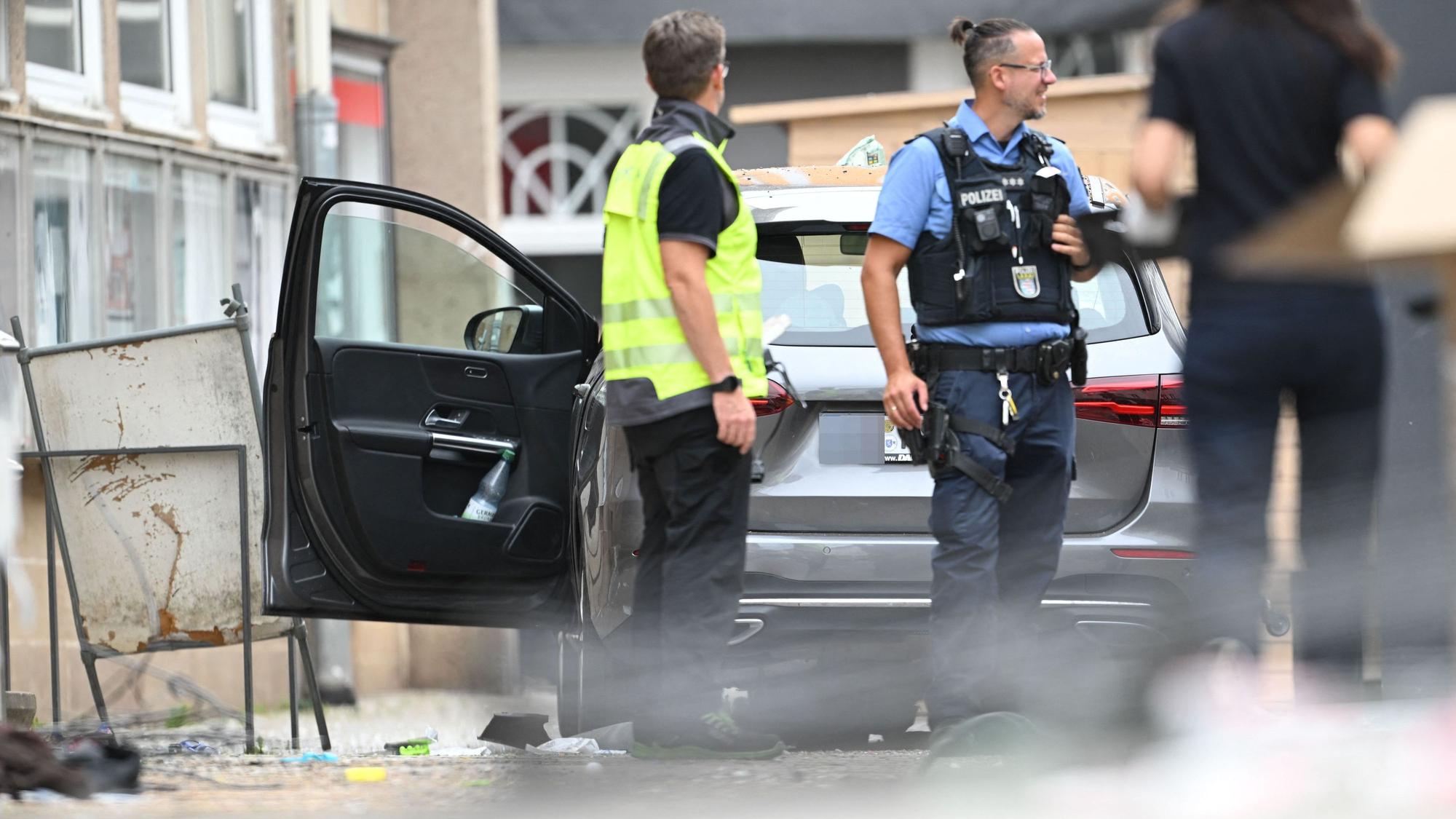 Ein Polizist und ein Mitarbeiter der DEKRA stehen vor einem Fahrzeug. Ein Autofahrer raste am Vormittag mit hoher Geschwindigkeit durch die Fußgängerzone und verletzte dabei mehrere Menschen.