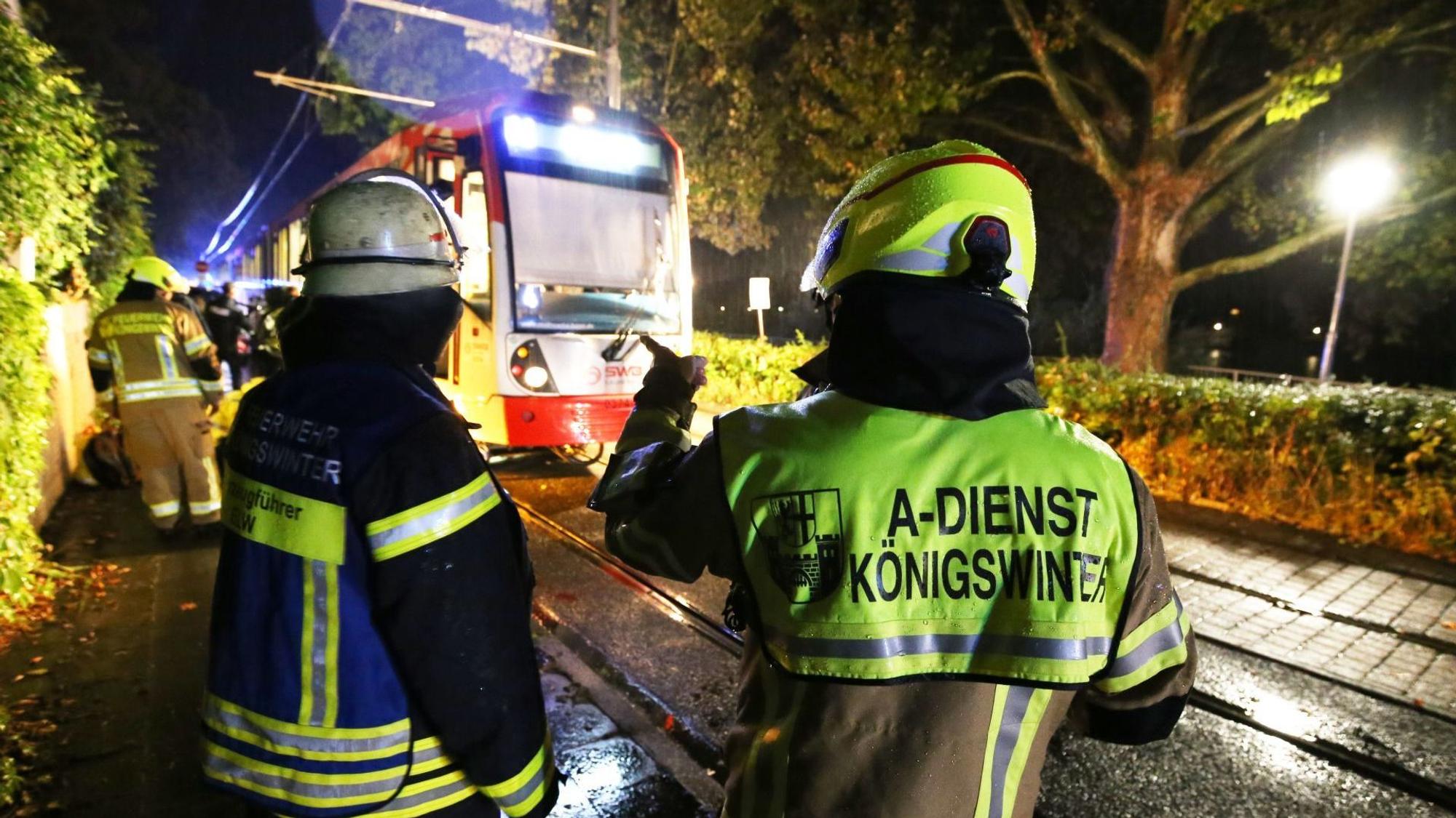 Feuerwehrleute stehen vor einer Straßenbahn, unter der ein Fahrrad eingeklemmt ist.