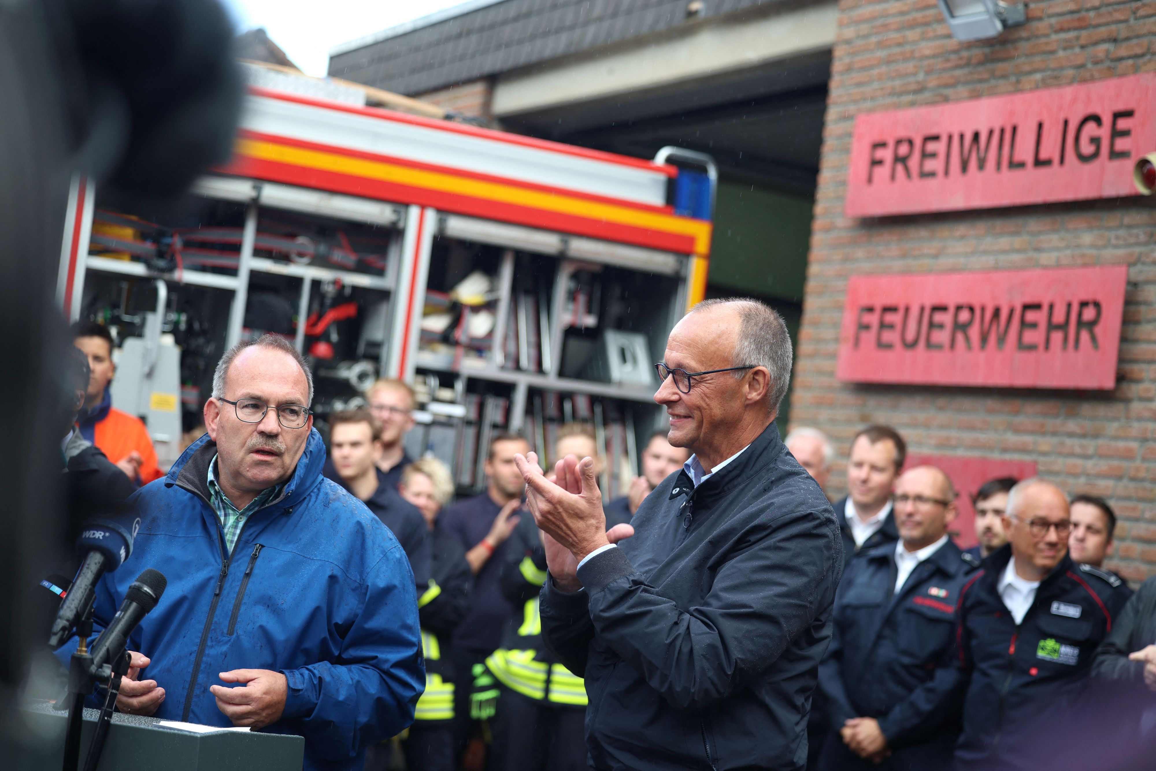 Ralf Nolten (l, CDU), Landrat des Kreises Düren, spricht bei einem Statement in Hürtgenwald-Gey neben Bundeskanzler Friedrich Merz (M, CDU).
