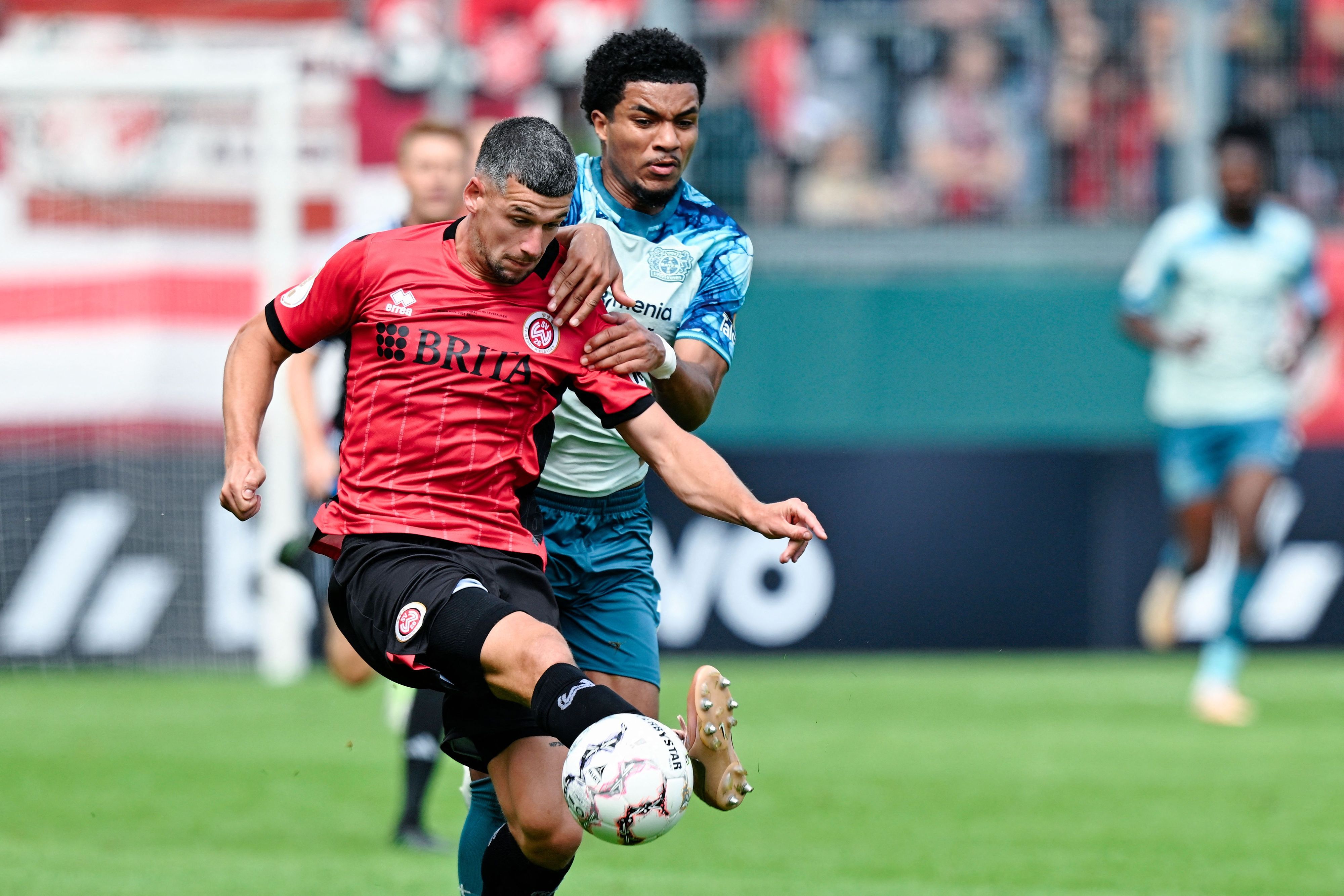 22.08.2026, Hessen, Wiesbaden: Fußball, Männer: DFB-Pokal, SV Wehen Wiesbaden - Bayer Leverkusen, 1. Runde, BRITA-Arena. Max Brandt (l, SV Wehen Wiesbaden) und Malik Tillmann (Bayer 04 Leverkusen) kämpfen um den Ball. Foto: Uwe Anspach/dpa - WICHTIGER HINWEIS: Gemäß den Vorgaben der Bundesliga bzw. des DFB Deutscher Fußball-Bund ist es untersagt, in dem Stadion und/oder vom Spiel angefertigte Fotoaufnahmen in Form von Sequenzbildern und/oder videoähnlichen Fotostrecken zu verwerten bzw. verwerten zu lassen. +++ dpa-Bildfunk +++