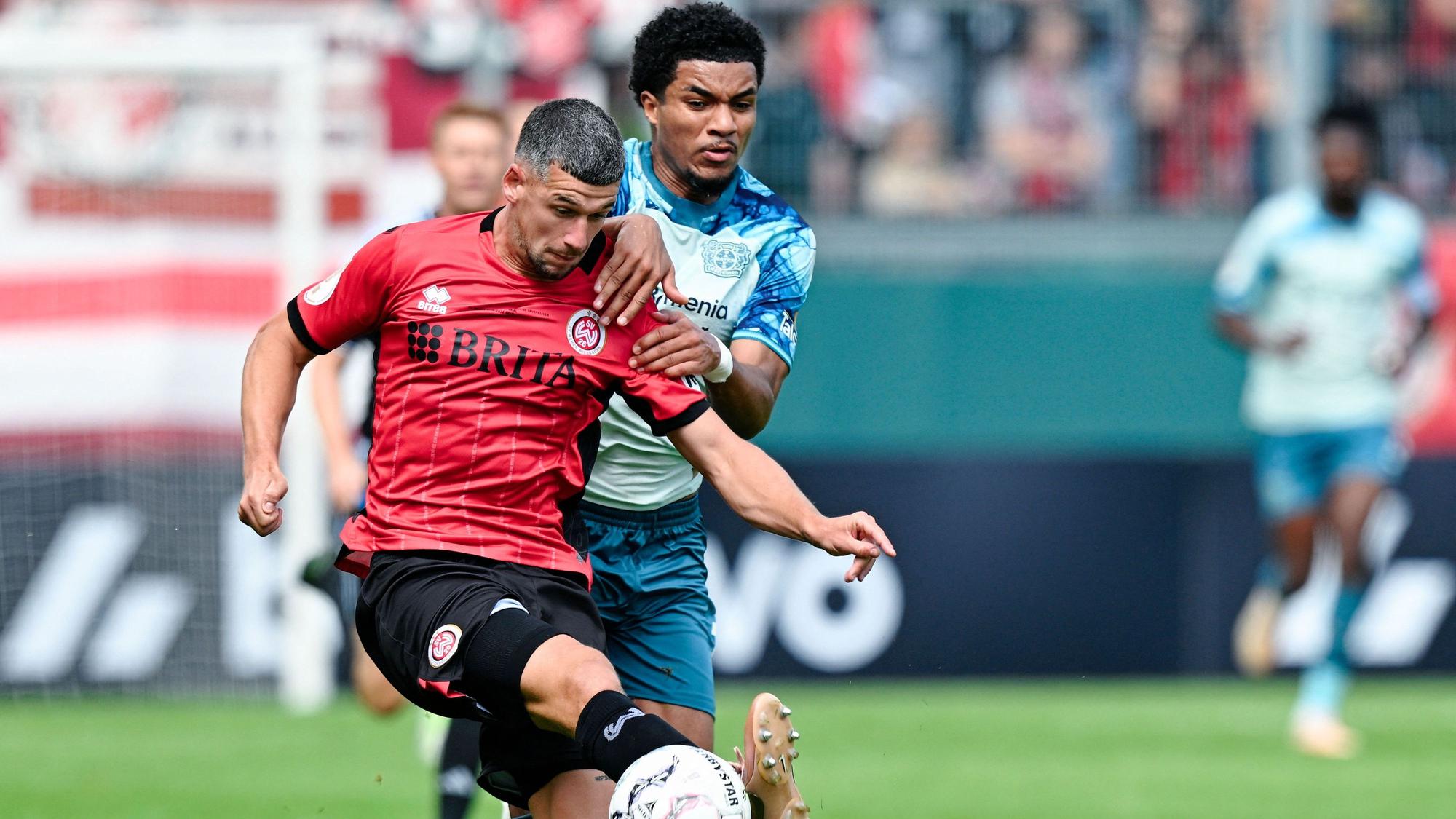 22.08.2026, Hessen, Wiesbaden: Fußball, Männer: DFB-Pokal, SV Wehen Wiesbaden - Bayer Leverkusen, 1. Runde, BRITA-Arena. Max Brandt (l, SV Wehen Wiesbaden) und Malik Tillmann (Bayer 04 Leverkusen) kämpfen um den Ball. Foto: Uwe Anspach/dpa - WICHTIGER HINWEIS: Gemäß den Vorgaben der Bundesliga bzw. des DFB Deutscher Fußball-Bund ist es untersagt, in dem Stadion und/oder vom Spiel angefertigte Fotoaufnahmen in Form von Sequenzbildern und/oder videoähnlichen Fotostrecken zu verwerten bzw. verwerten zu lassen. +++ dpa-Bildfunk +++