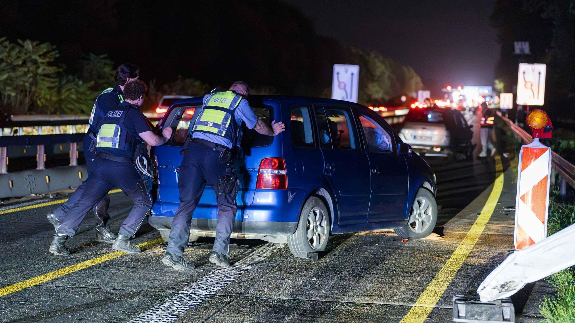 Polizisten schieben den verunfallten Wagen auf einer Autobahn.