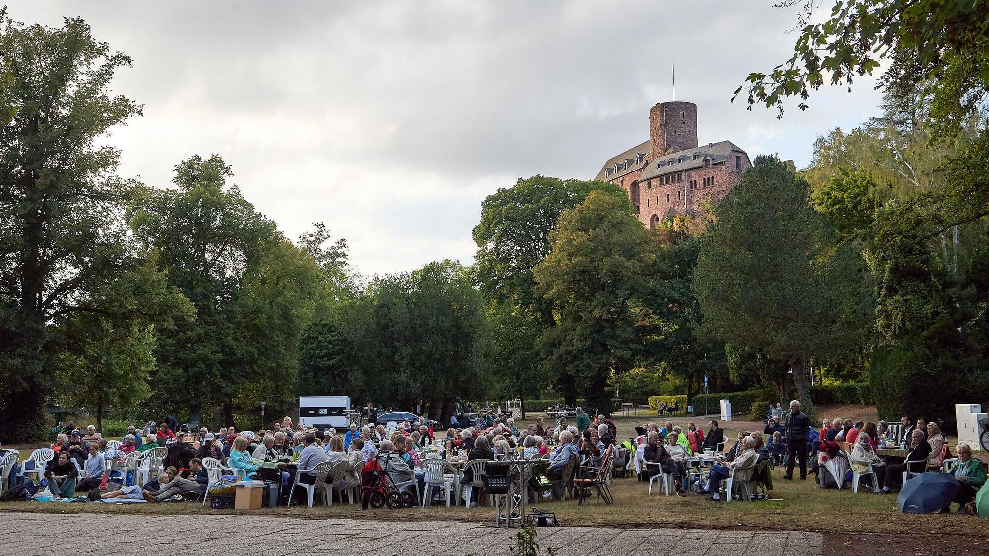 In Vordergrund sitzen die Besucher des Picknickkonzerts, im Hintergrund ragt die Burg Hengebach über ihnen.
