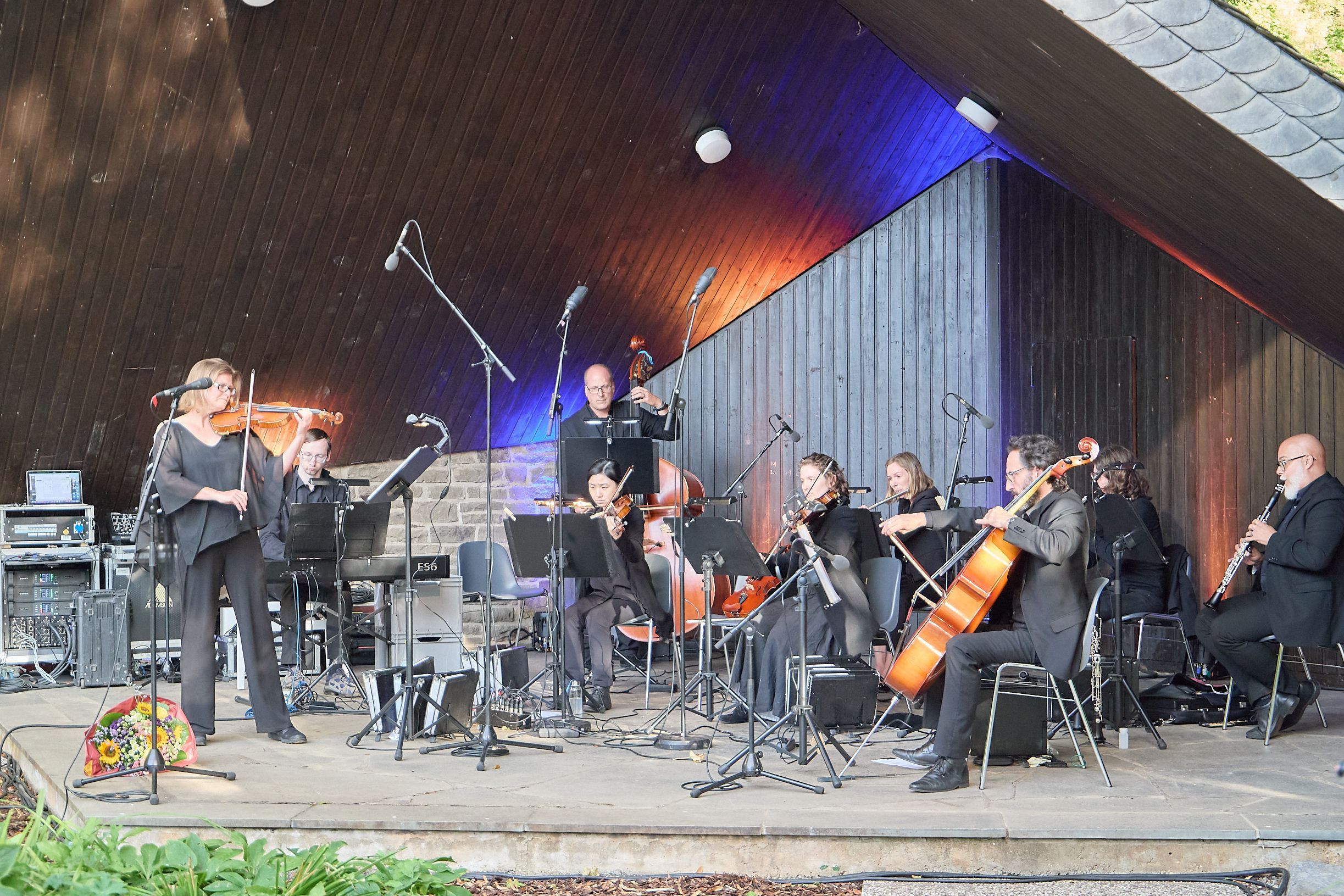 Das Orchester steht und sitzt auf einer Bühne.