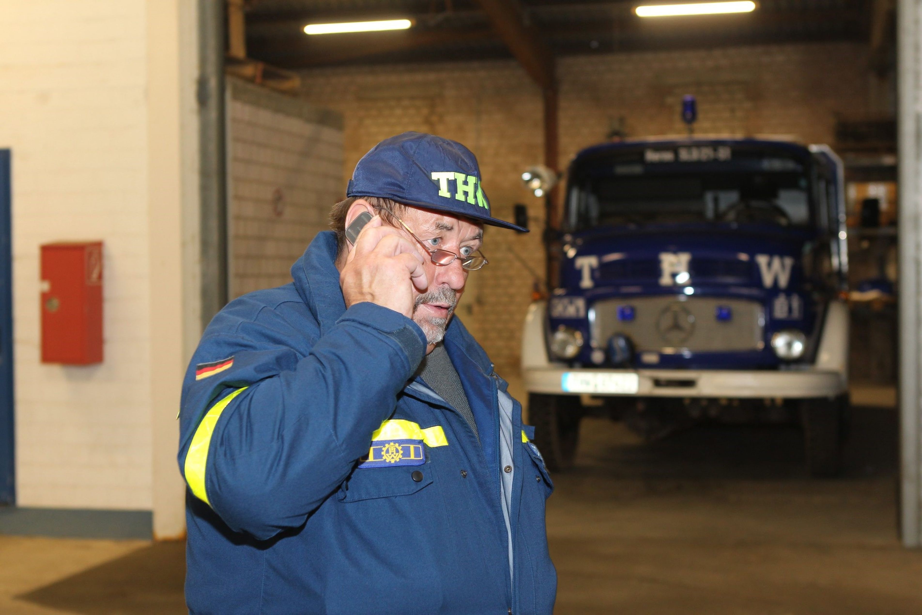 Richard Schwarzer trägt Jacke und Kappe des THW. Er telefoniert mit einem Mobiltelefon.