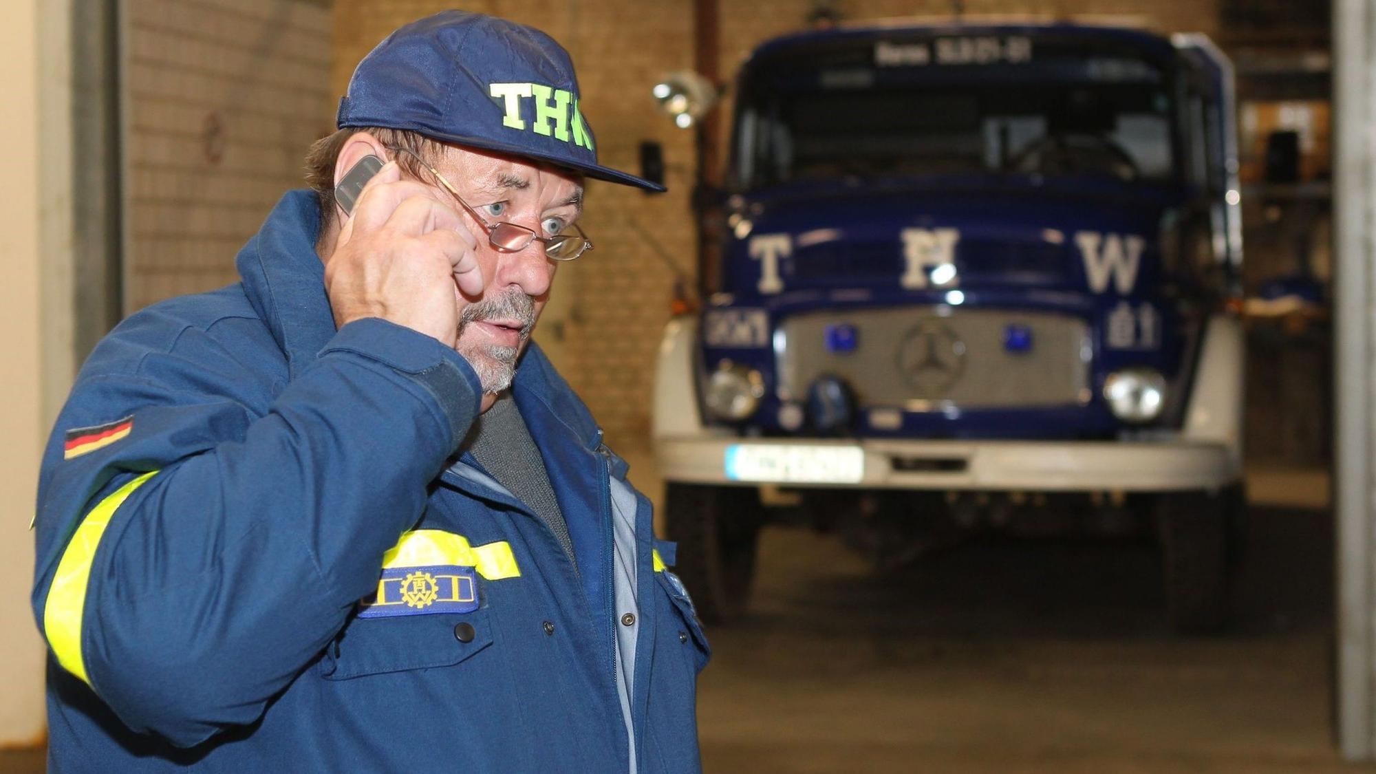 Richard Schwarzer trägt Jacke und Kappe des THW. Er telefoniert mit einem Mobiltelefon.