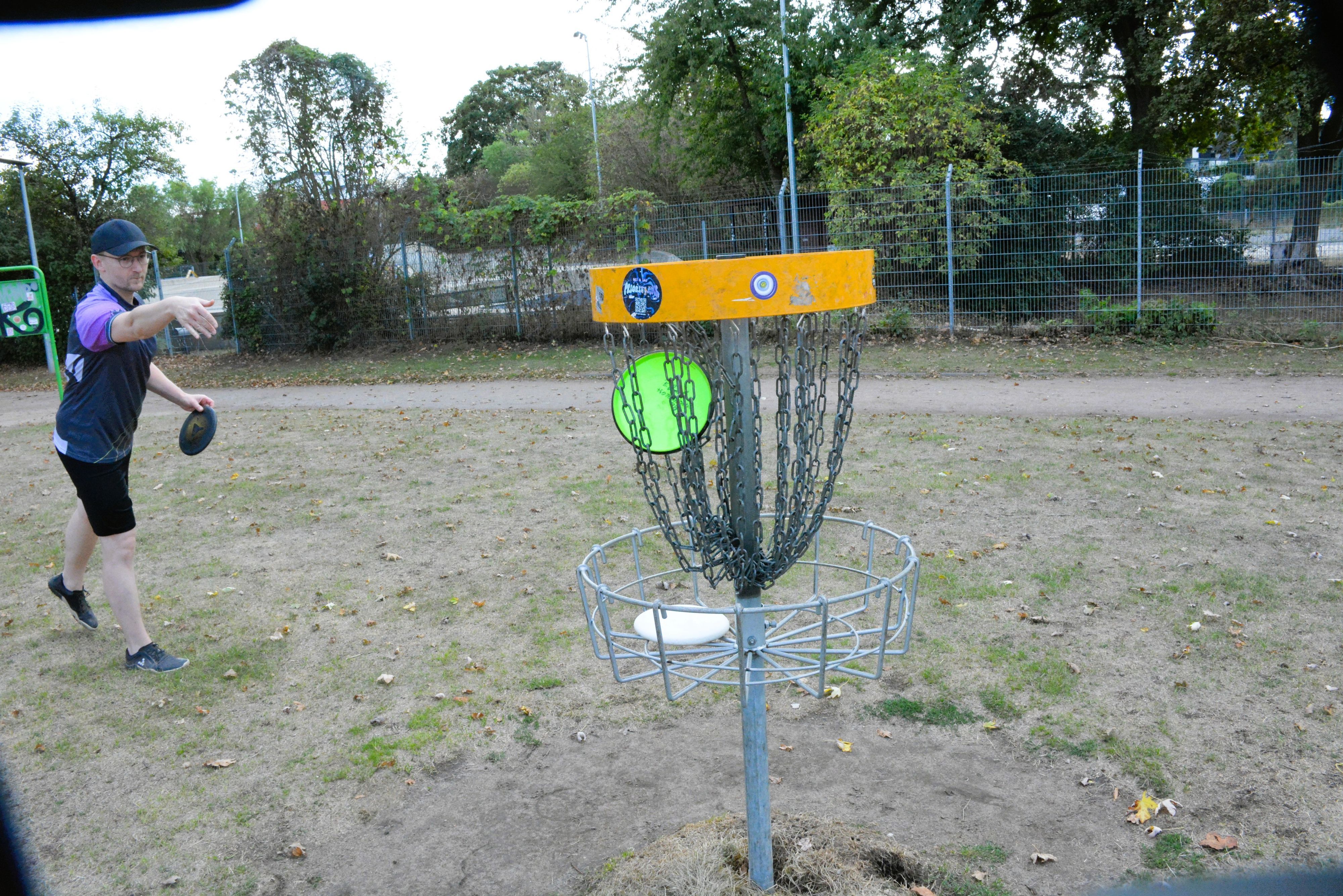 Benedikt Pöpsel wirft eine Discgolf-Scheibe in ein Kettengeflecht.