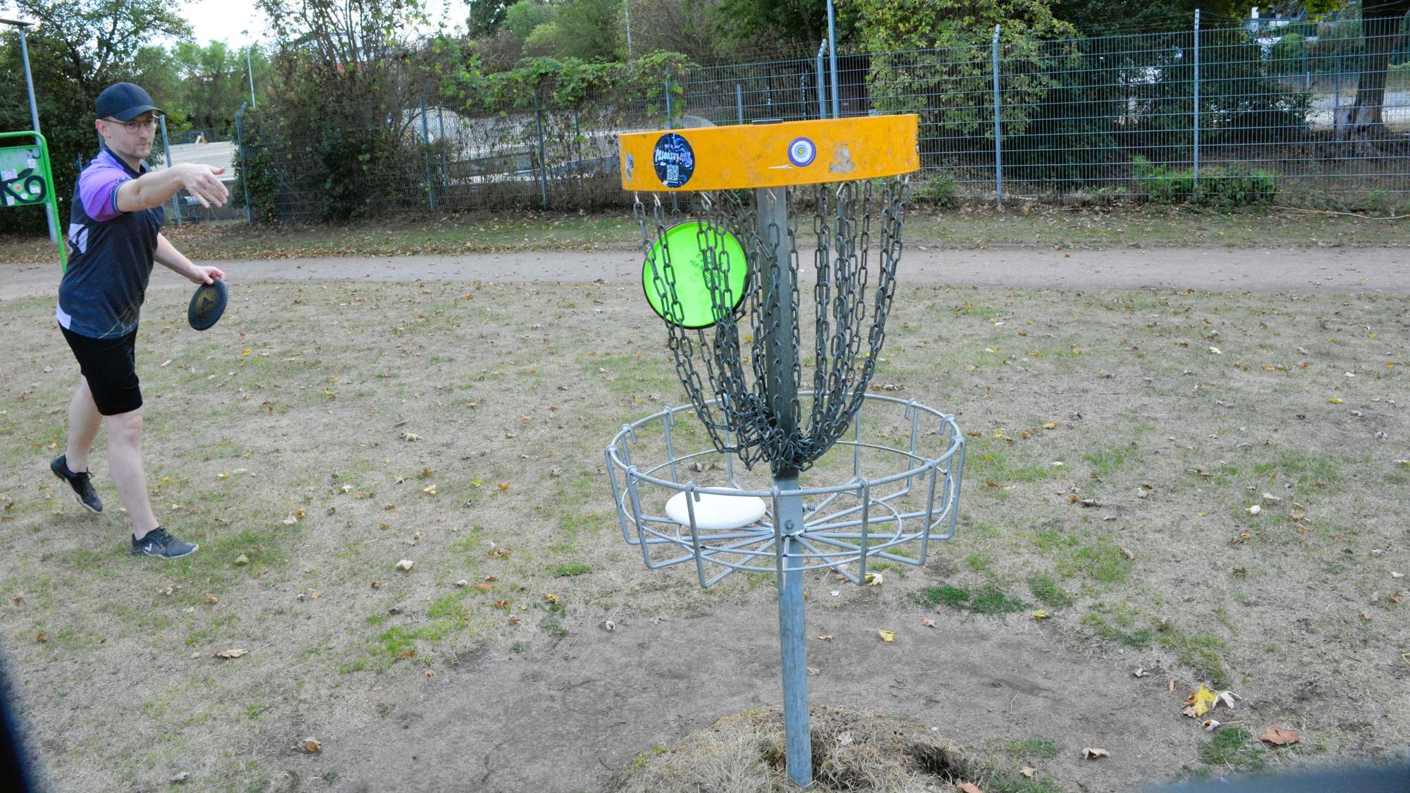 Benedikt Pöpsel wirft eine Discgolf-Scheibe in ein Kettengeflecht.