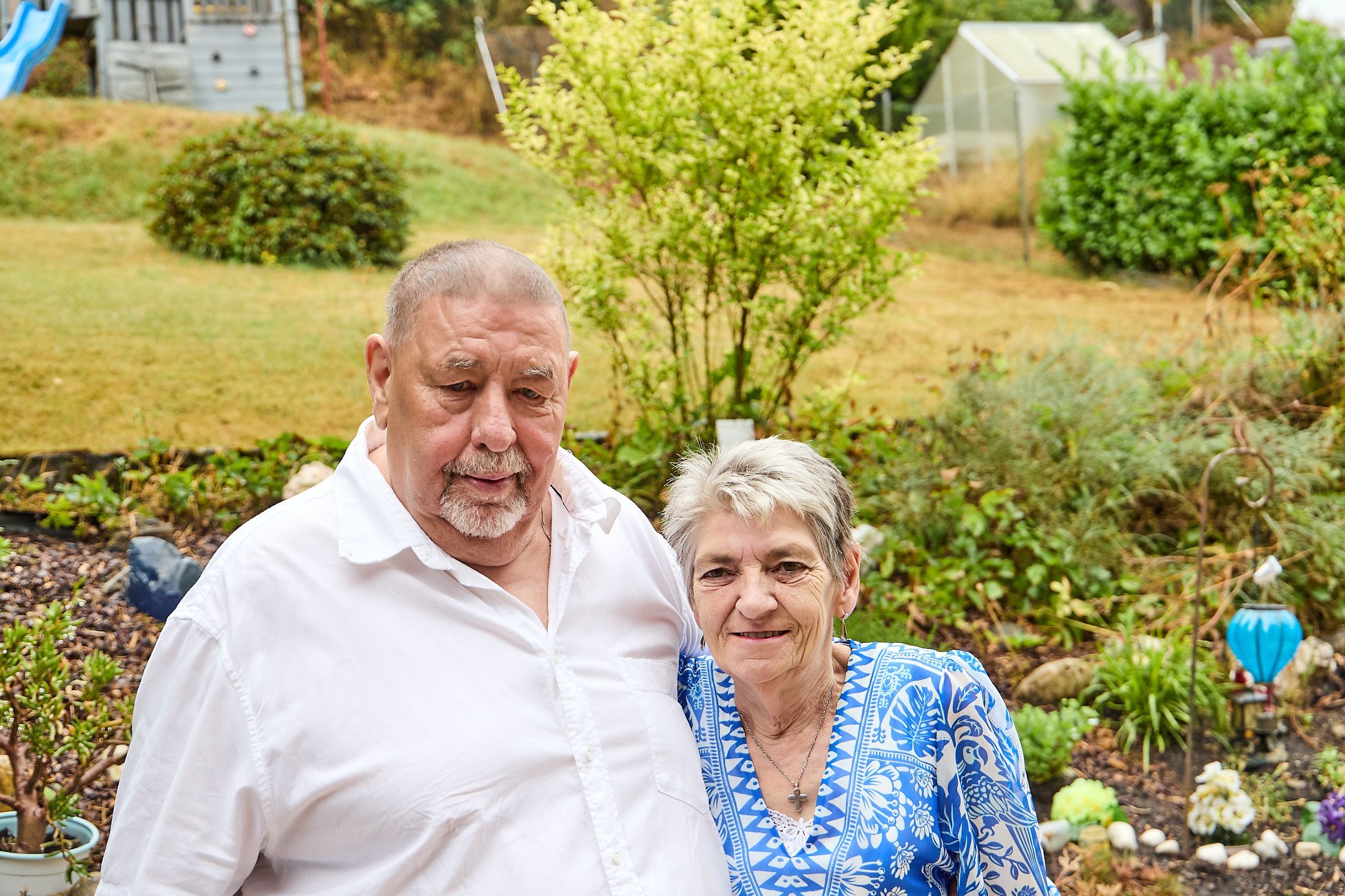 Richard Schwarzer und Gabrielle Hebertz stehen Arm in Arm vor einem Bett in ihrem Garten in Hellenthal.