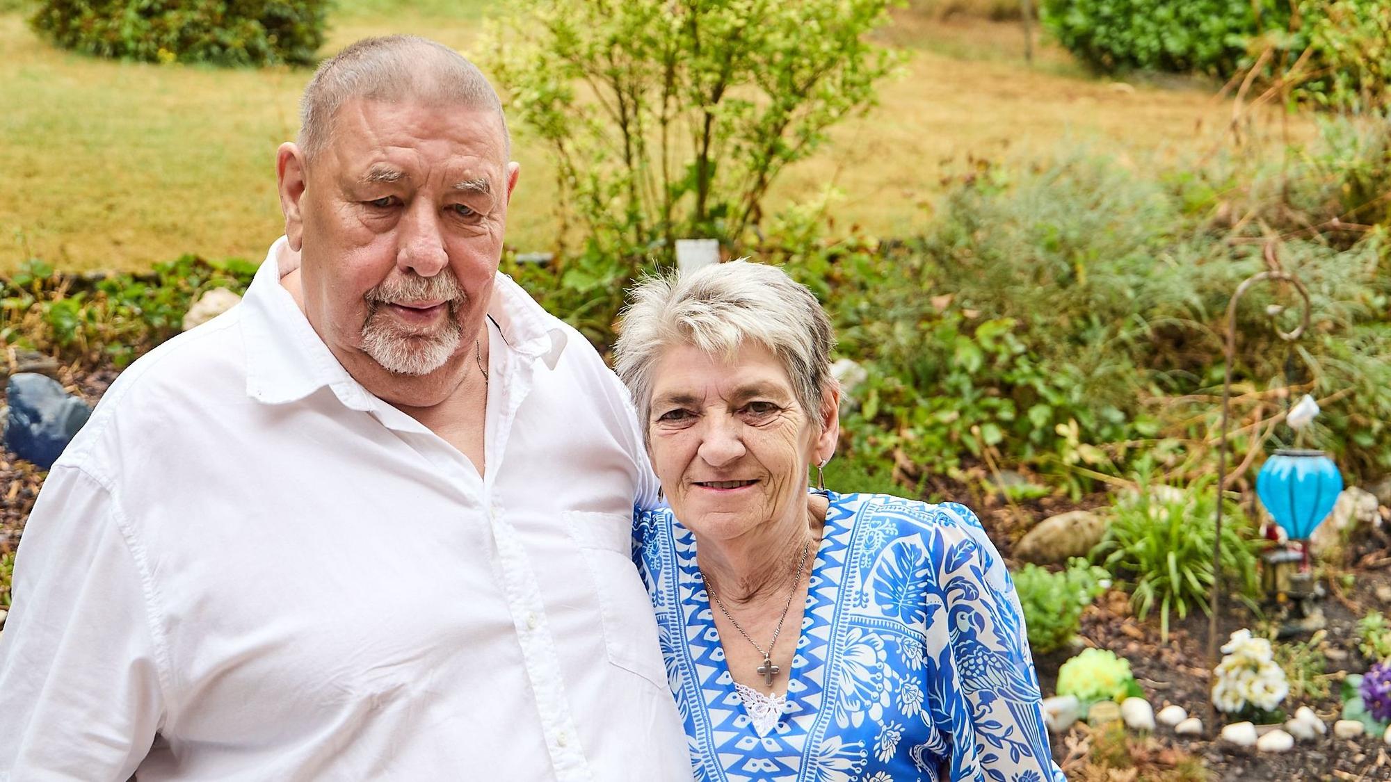 Richard Schwarzer und Gabrielle Hebertz stehen Arm in Arm vor einem Bett in ihrem Garten in Hellenthal.