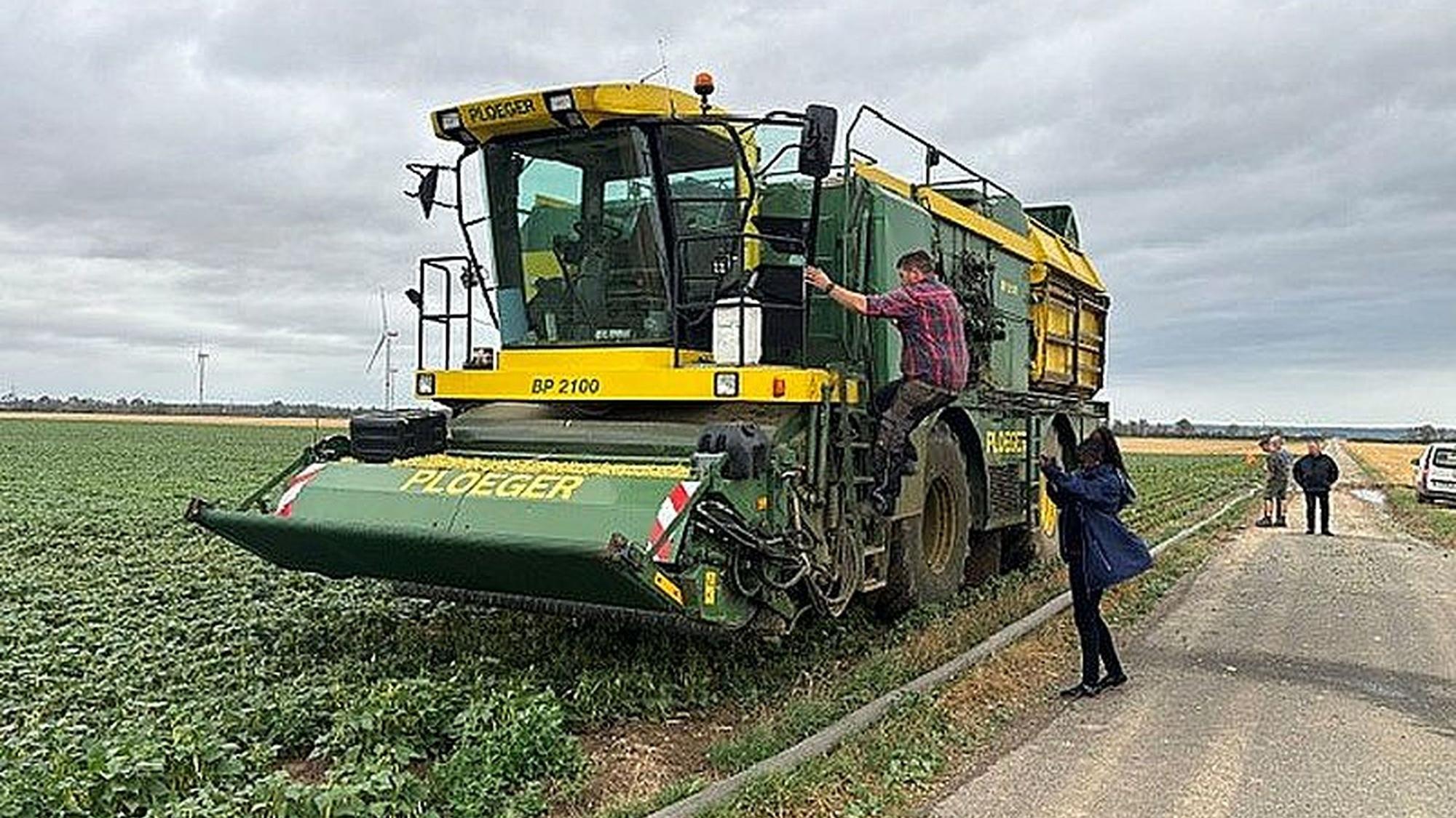 Bridgit Obuya steht auf einem Feldweg neben einer Erntemaschine, auf die gerade ein Mann steigt.