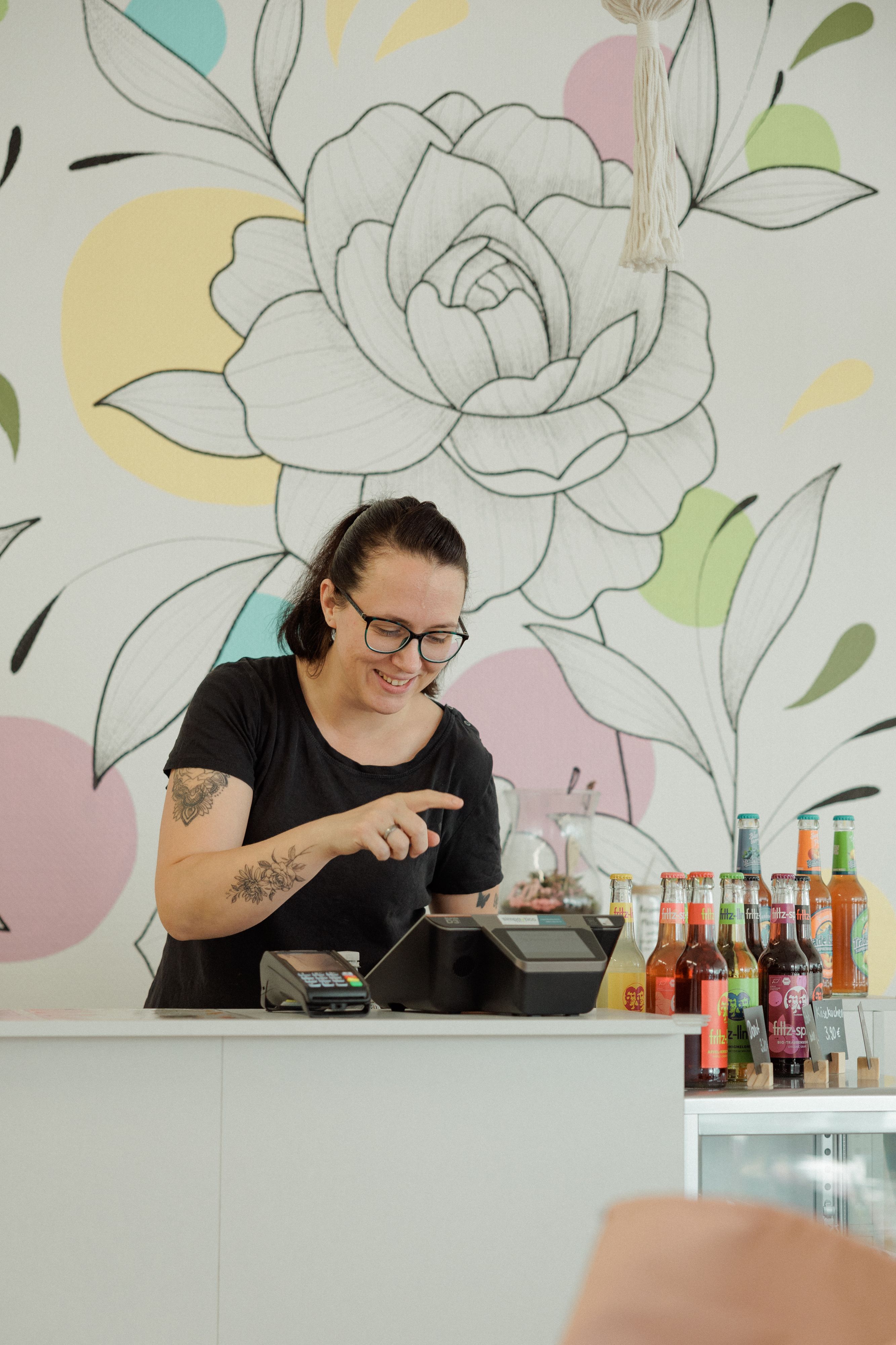 Zu sehen ist eine Frau, die hinter einem Café-Tresen steht und etwas in das Kassensystem eingibt.