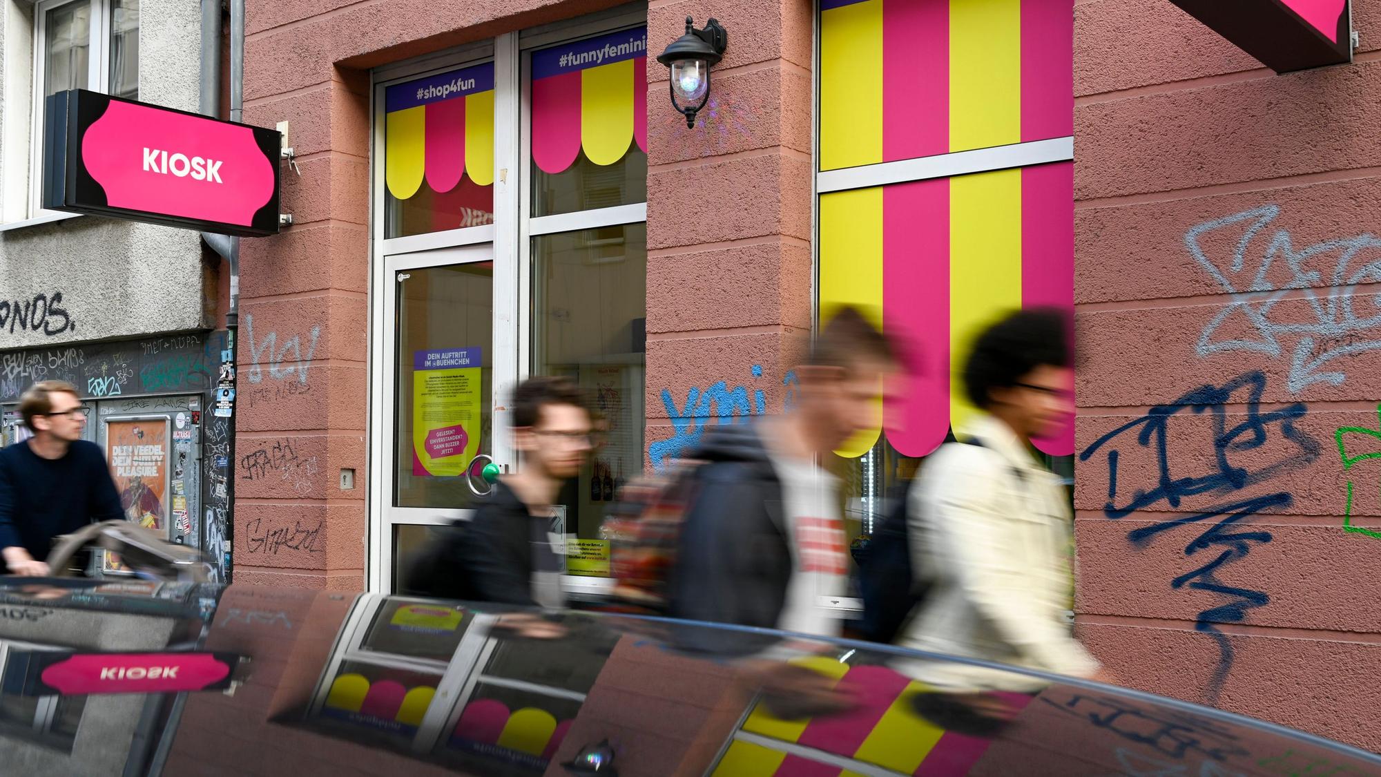 Der neue Kiosk in der Kyffhäuserstraße 15 hat am vergangenen Wochenende seine Eröffnung gefeiert. Die Schilder sind pink, es laufen mehrere Menschen daran vorbei.