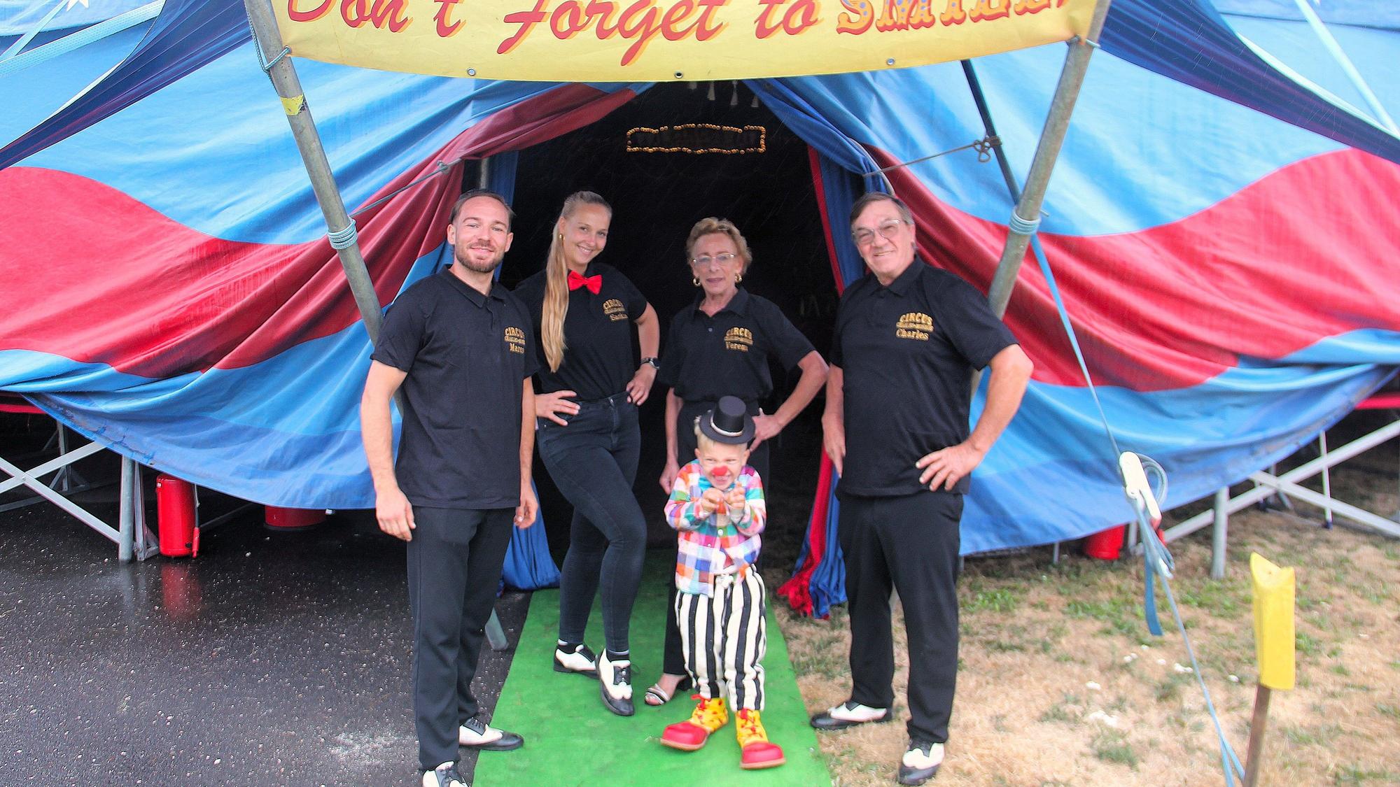 Zwei Frauen und zwei Männer stehtn neben einem Kind, das als Clown verkleidet ist, vor einem Zirkuszelt.