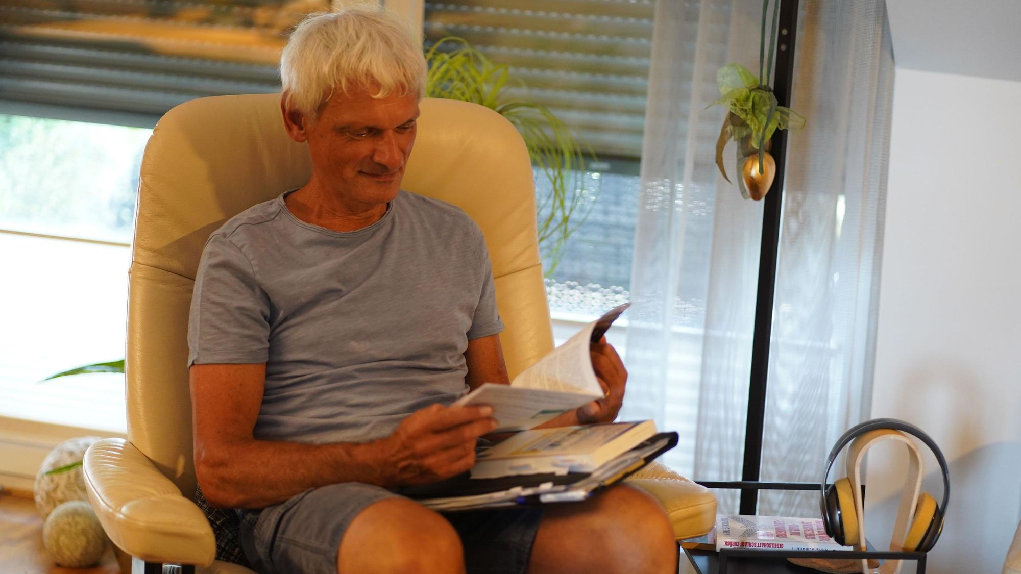 Das Foto zeigt einen Mann in einem Sessel, der in einem Buch liest.