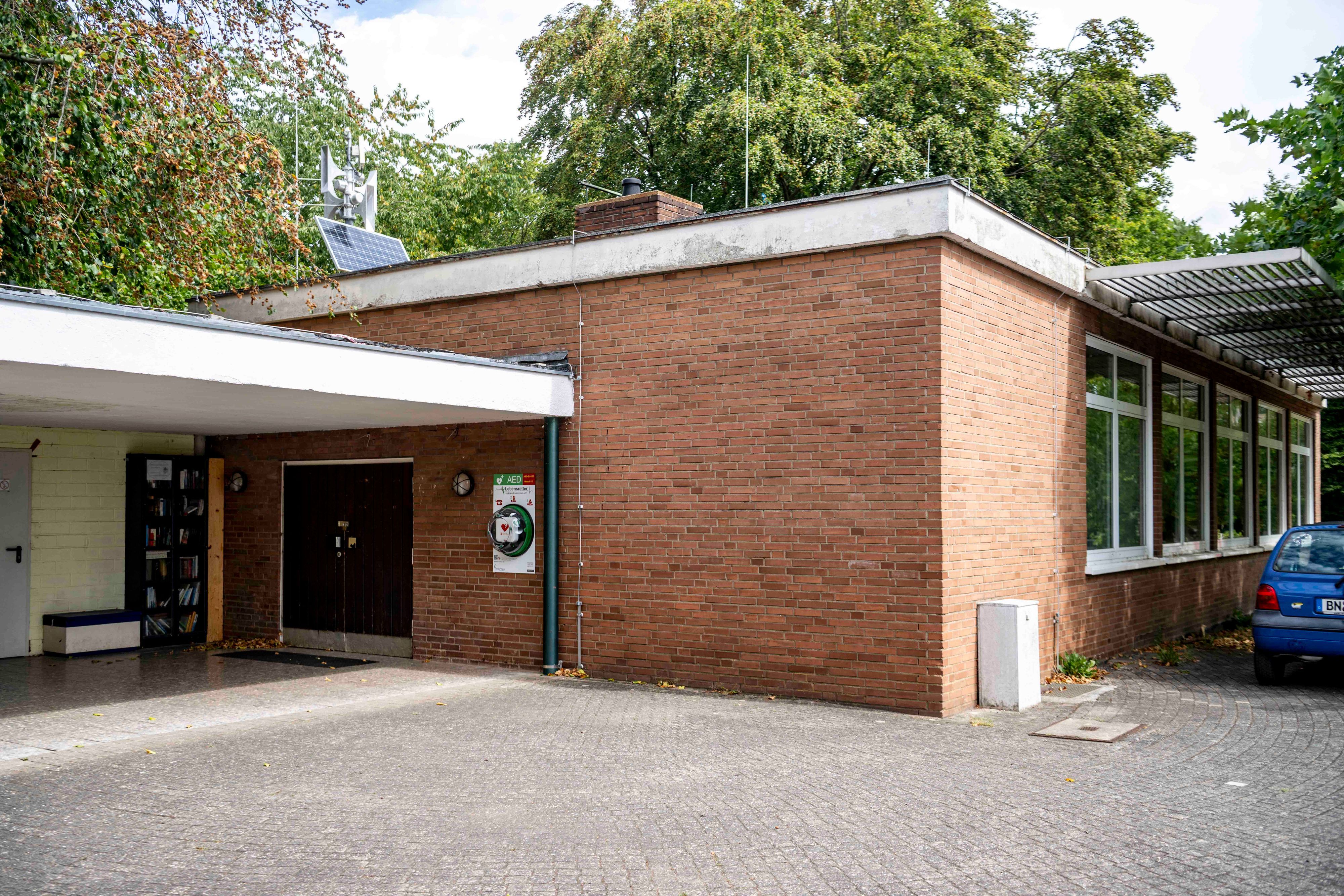 Das Dorfgemeinschaftshaus ist ein Flachbau, der Eingang ist überdacht. Hinter dem Gebäude stehen Bäume.