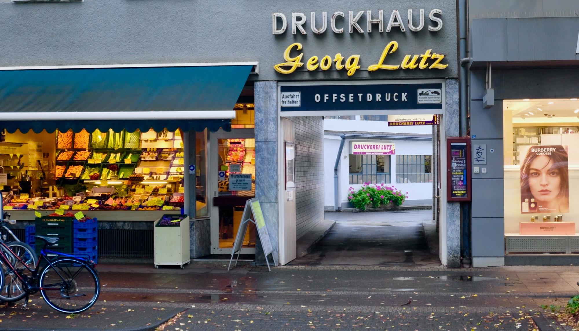 Neben einem Gemüseladen liegt die Einfahrt zum Druckhaus Georg Lutz.