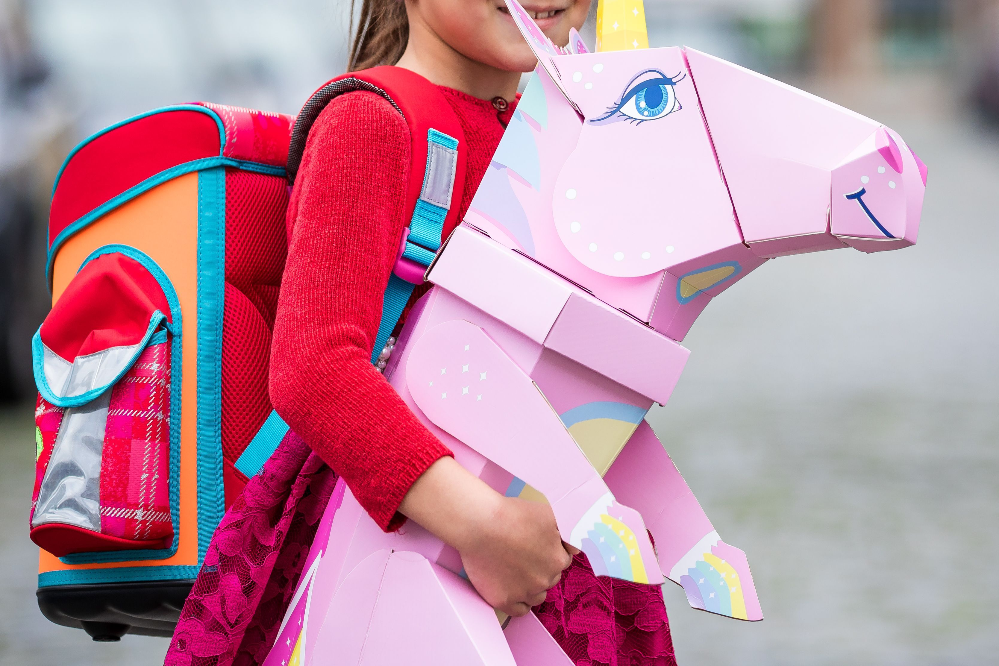 Eine Erstklässlerin steht mit Ranzen und Einhorn-Schultüte am Tag ihrer Einschulung vor der Schule.