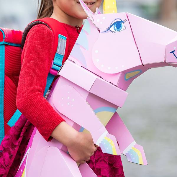 Eine Erstklässlerin steht mit Ranzen und Einhorn-Schultüte am Tag ihrer Einschulung vor der Schule.