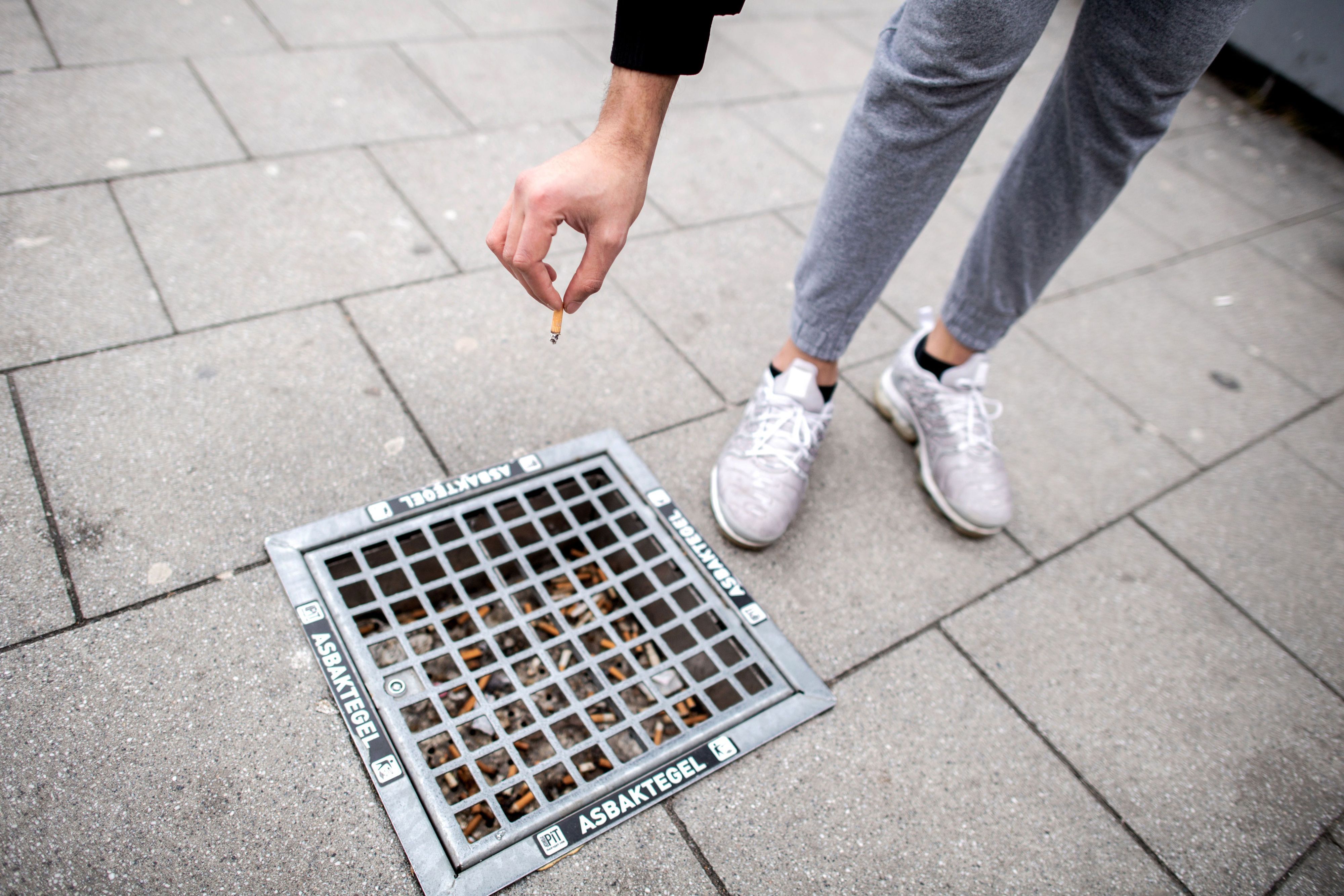 Ein Mann wirft einen Zigarettenstummel in einen Bodenaschenbecher in der Innenstadt.