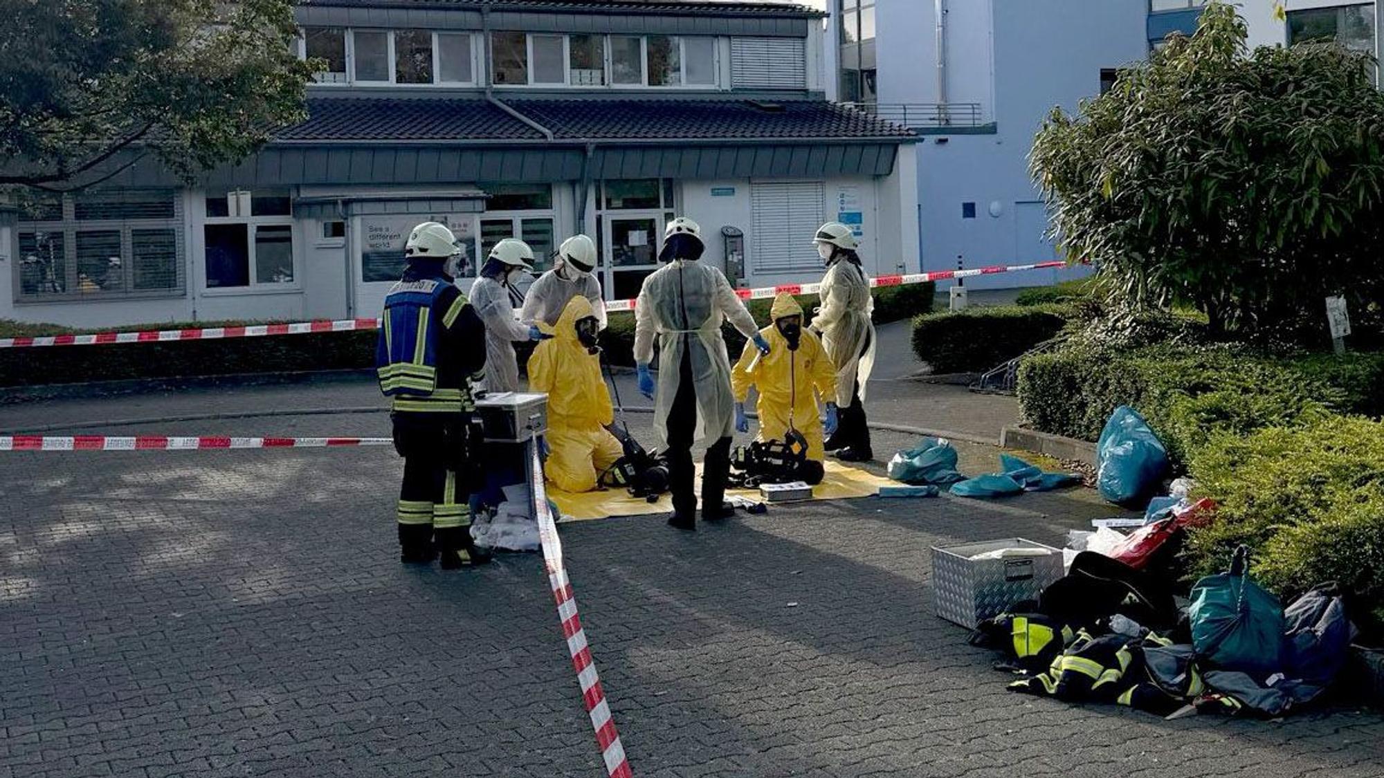 Vor einem Krankenhaus stehen Feuerwehrleute, zum Teil in Schutzanzügen.