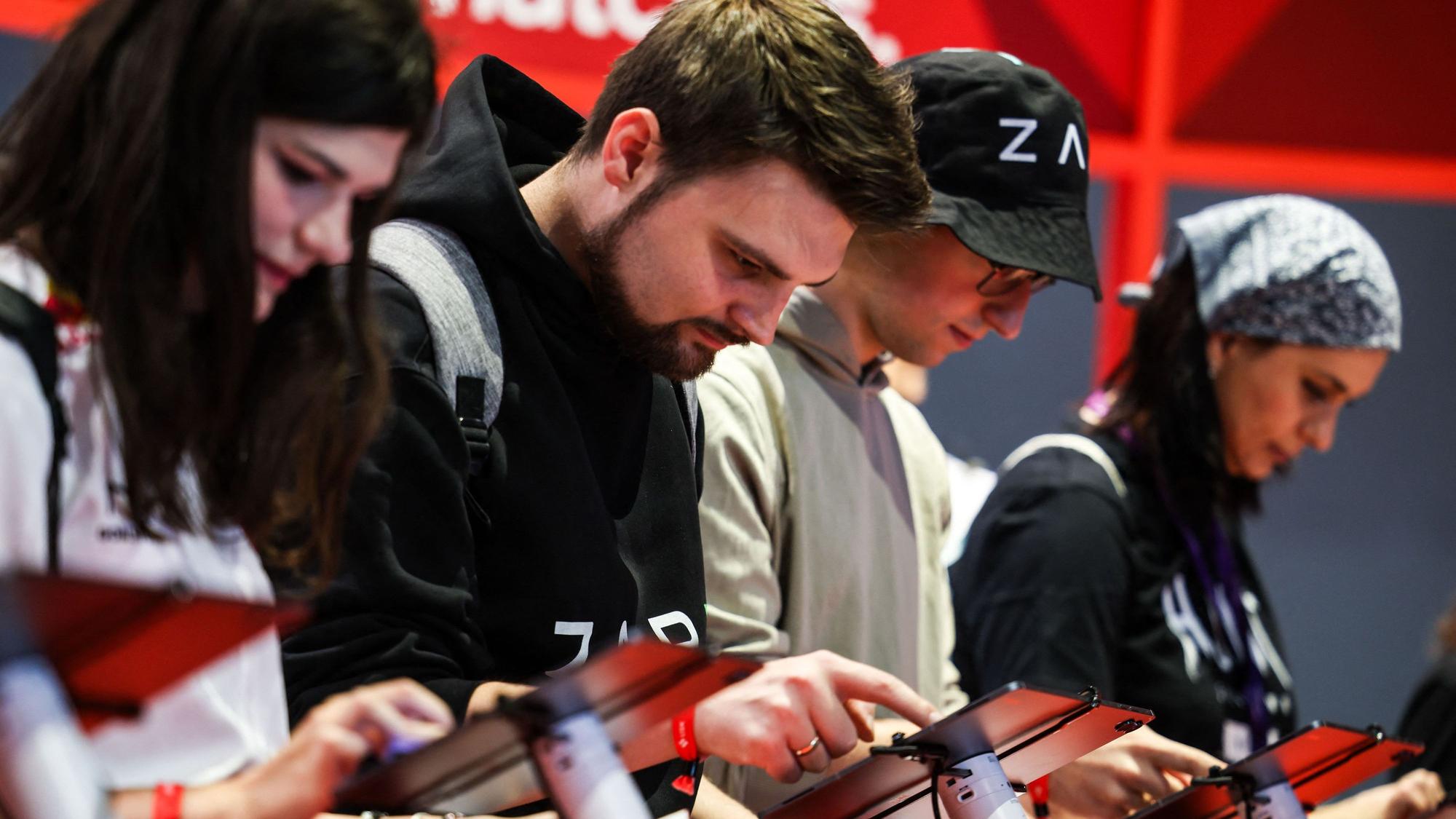 Besucher der Messe Gamescom stehen an Tablets und spielen ein Videospiel.