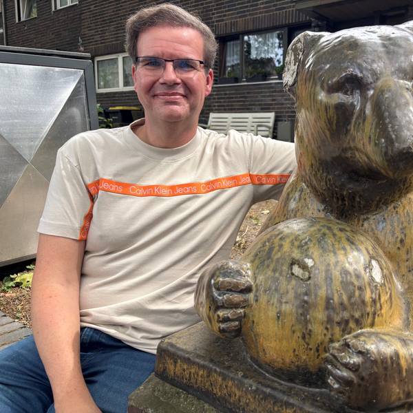 Auf dem Bild ist ein Mann im T-Shirt zu sehen, er umarmt eine keramische Bärenskulptur.